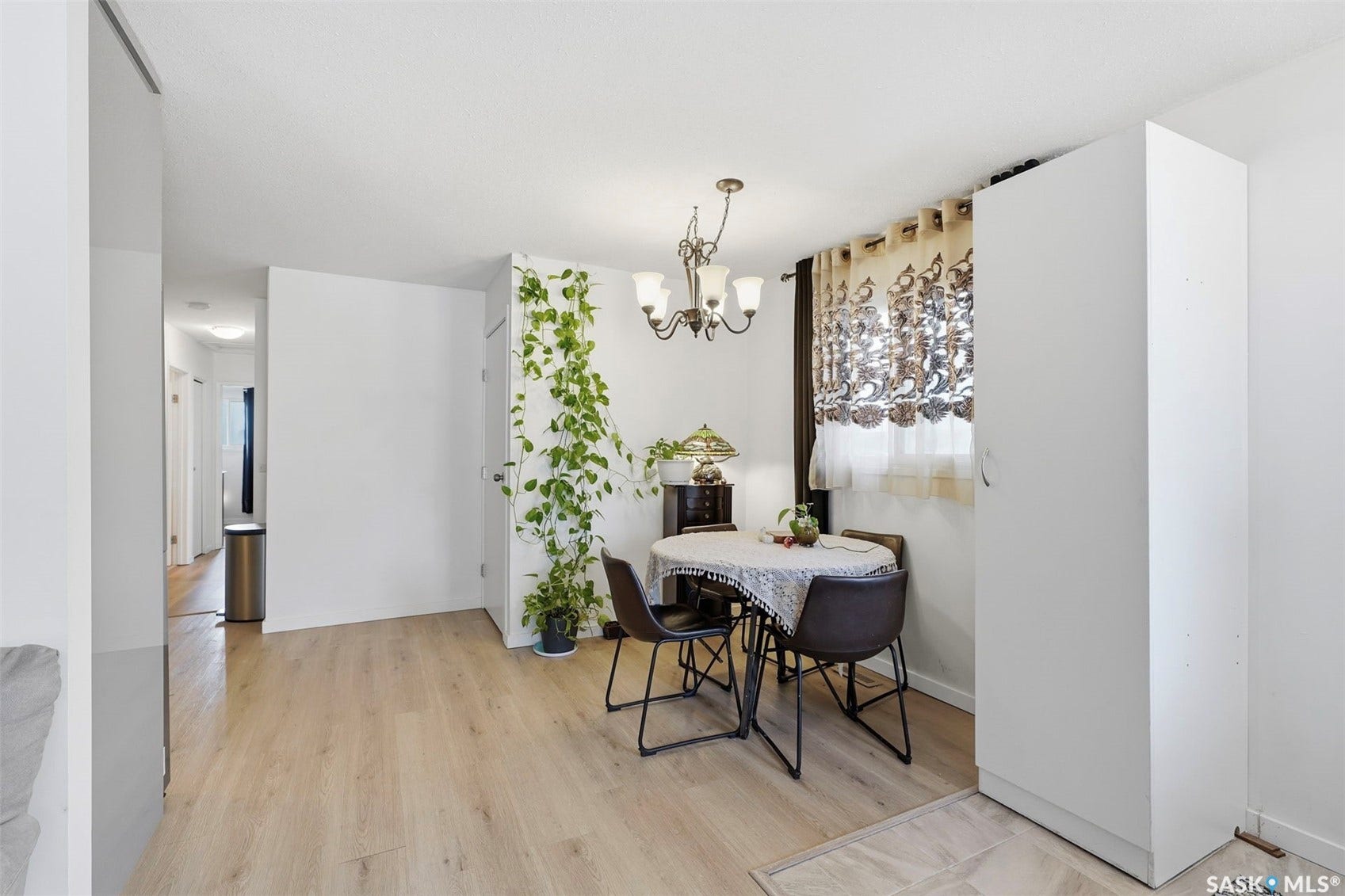 Light wood-finish flooring, white walls, and a multi-light chandelier