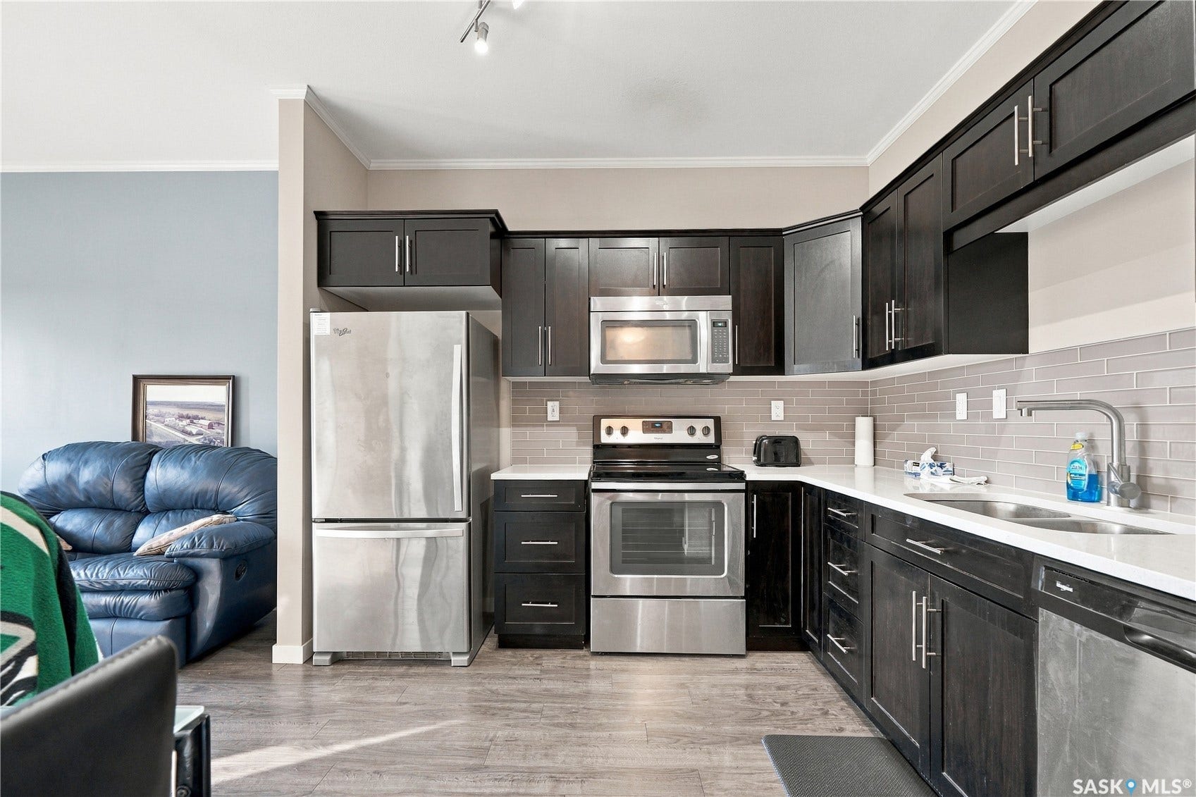 Kitchen featuring stainless steel appliances, dark wood-finish cabinetry, solid surface countertops, and a subway tile backsplash