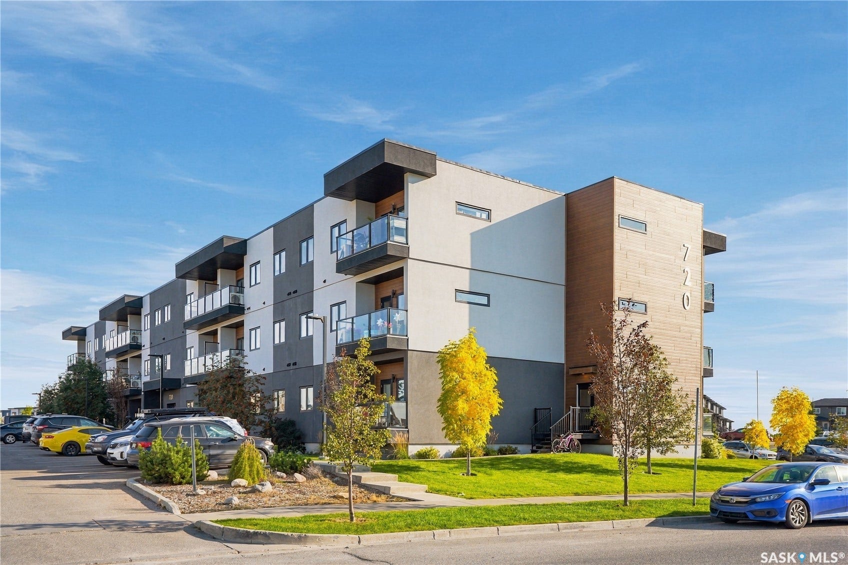 Modern multi-story building featuring a facade with dark gray and white panels, wood-finish accents, and multiple balconies with glass railings