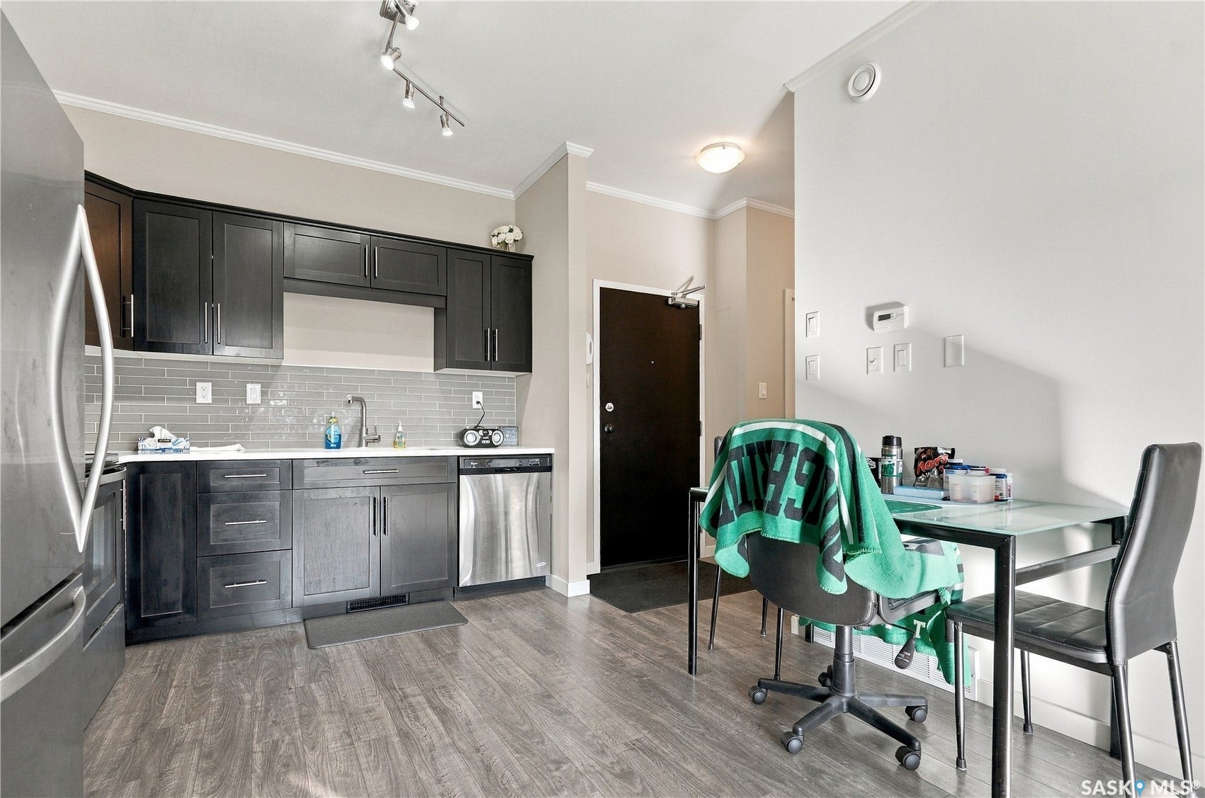 Kitchen featuring dark wood-finish cabinetry, stainless steel appliances, grey subway tile backsplash, and wood-finish flooring