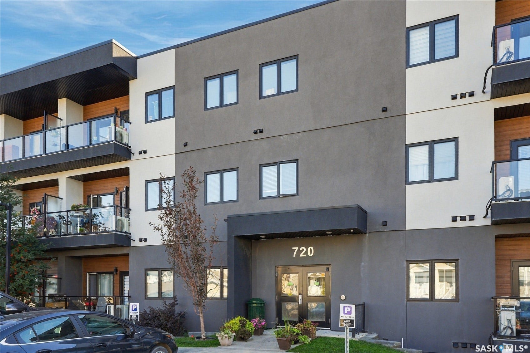 Modern multi-story building featuring a facade with mixed siding, multiple balconies with glass railings, and a prominent main entrance