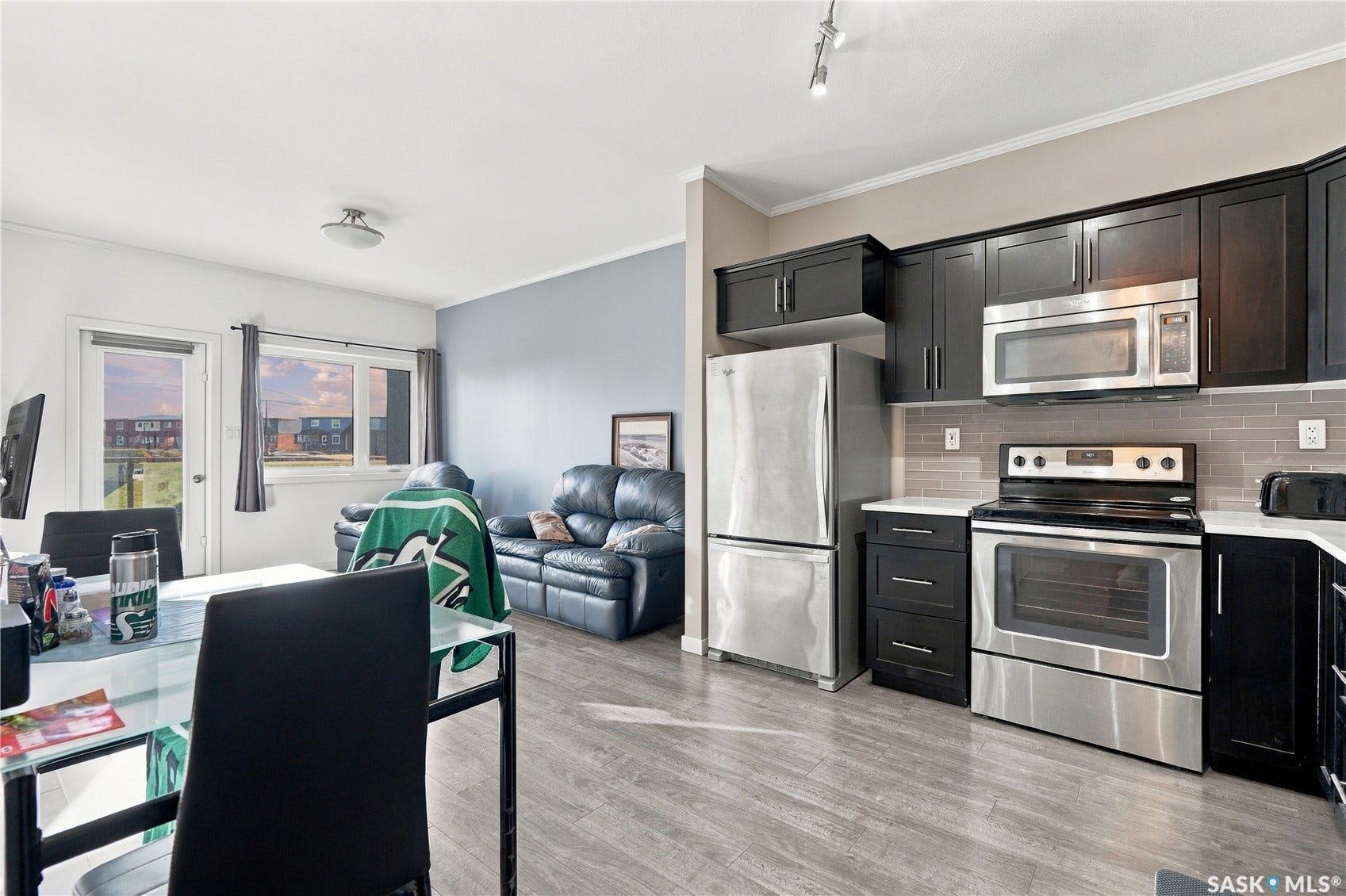 Open-concept living area with wood-finish flooring, dark wood cabinetry, stainless steel appliances, and a tiled backsplash