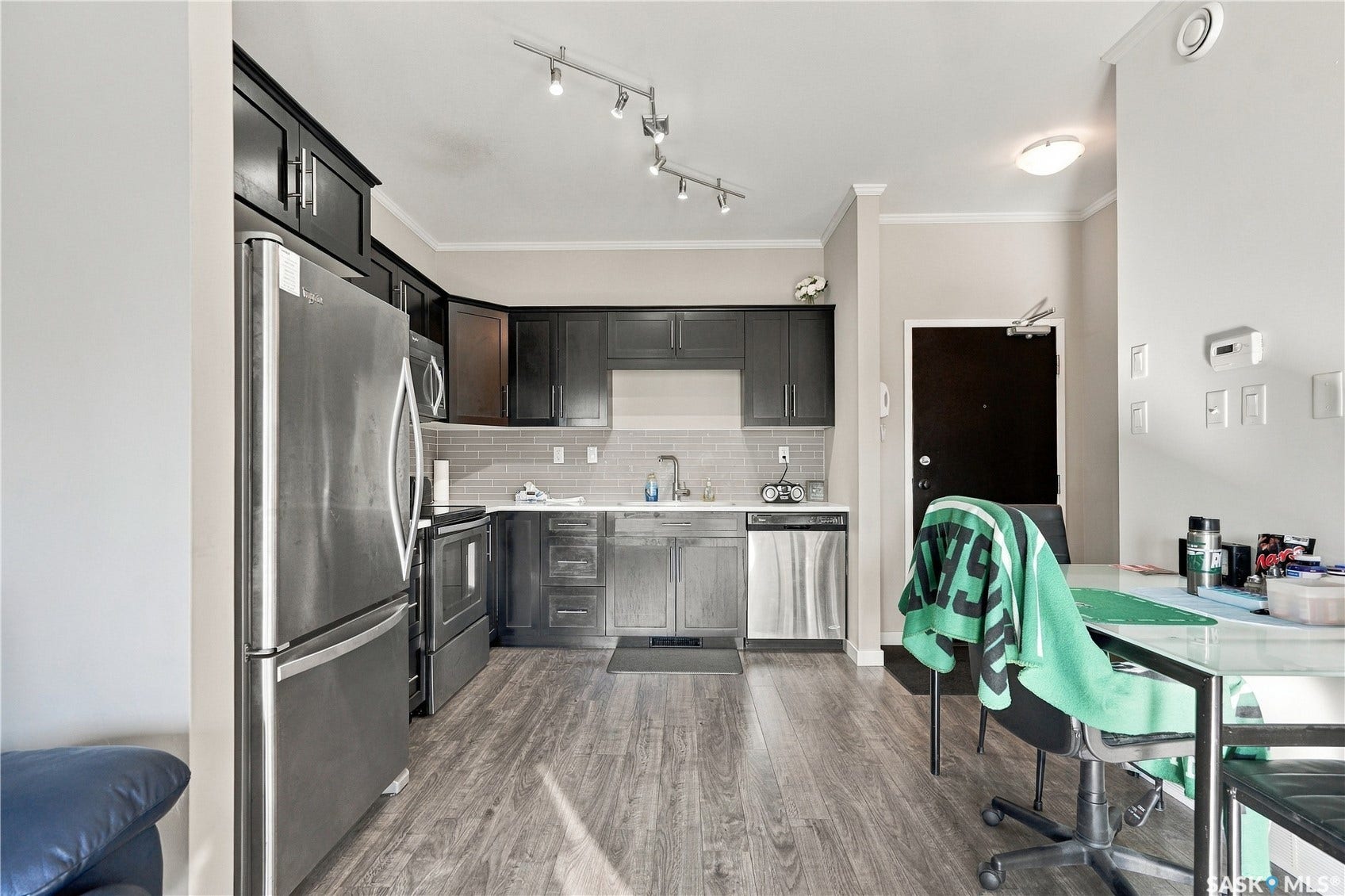 Kitchen featuring dark wood cabinetry, stainless steel appliances, a light-toned tile backsplash, and wood-finish flooring