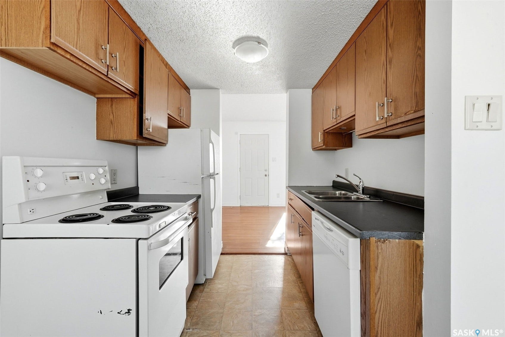 Galley kitchen with wood cabinetry, white appliances, and a compact dishwasher
