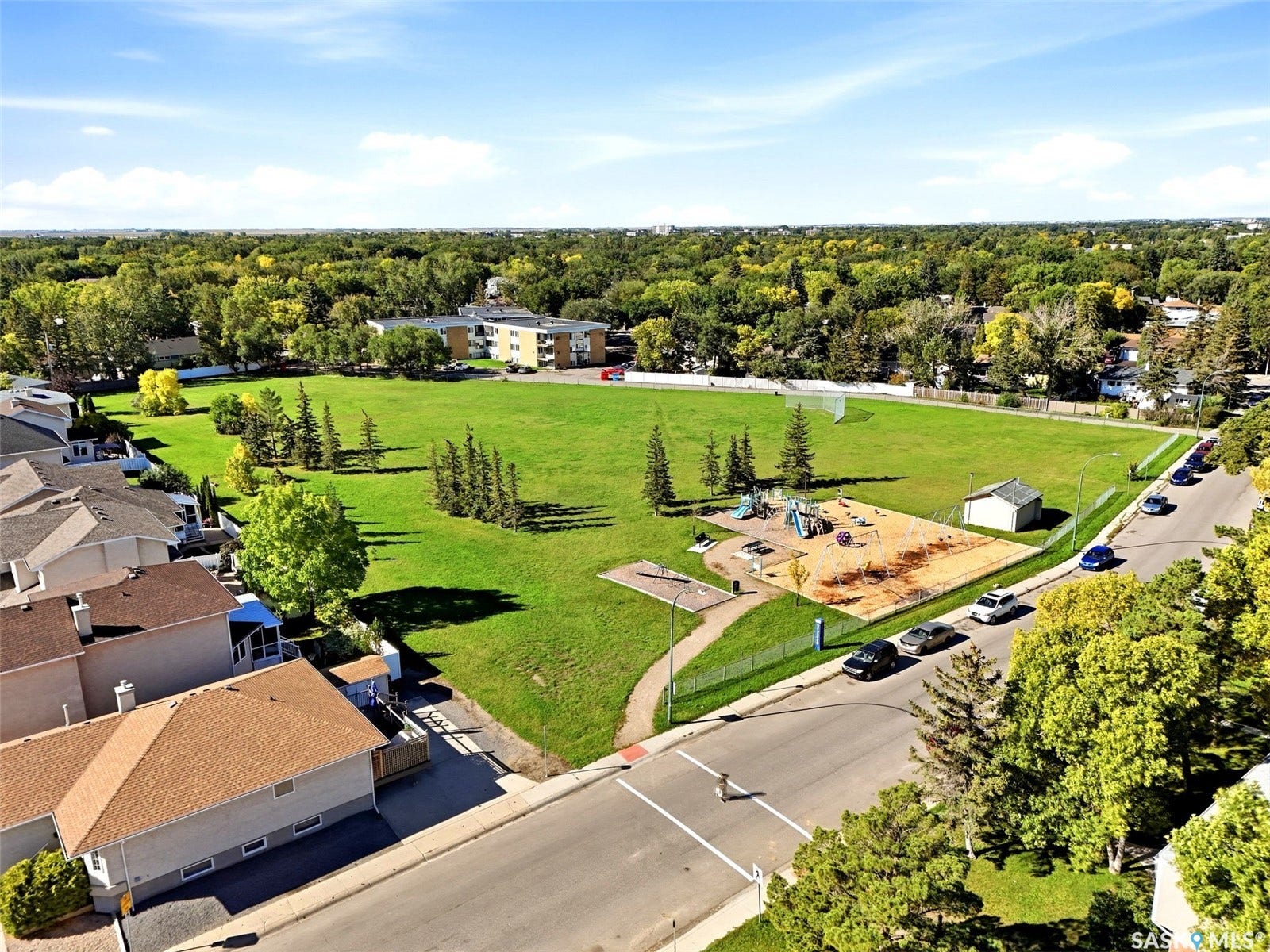 Expansive green space with mature trees, a dedicated playground area, a soccer goal, and paved walking paths