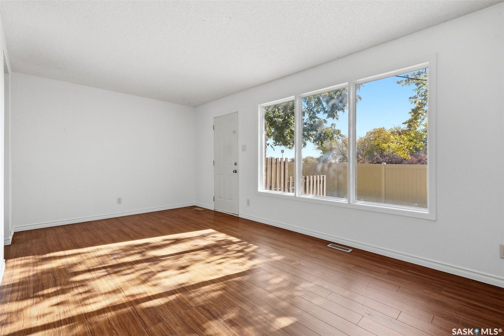 Wood-finish flooring with white baseboards, a three-pane window, and a white interior door