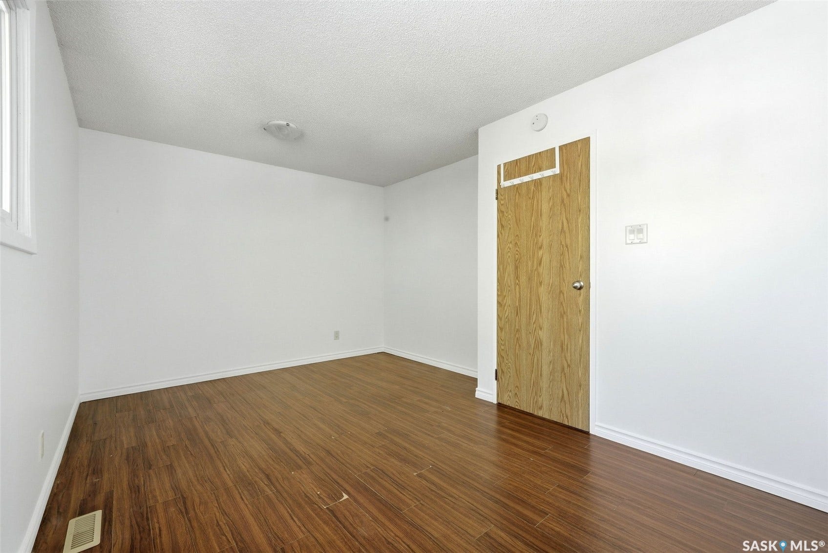 Room featuring wood-finish flooring, white walls, and a single window