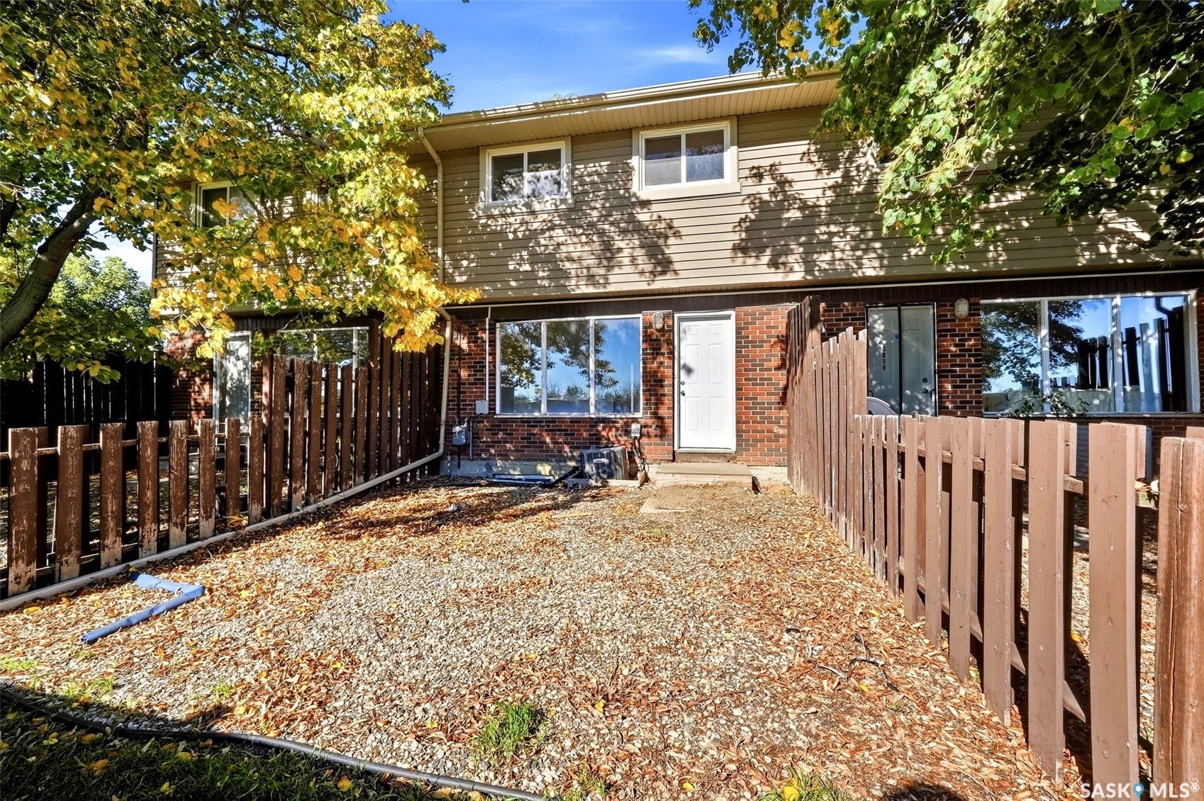 Brown wood-paneled fence enclosing a gravel and leaf-covered yard