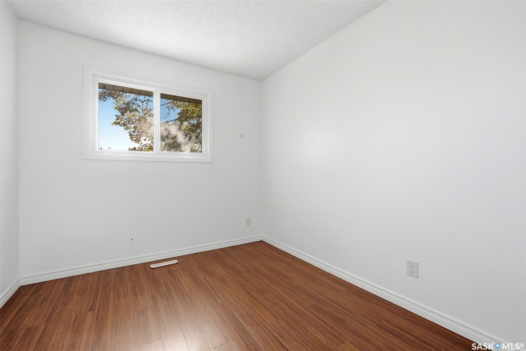 Room featuring wood-finish flooring, white walls, and a window with white trim