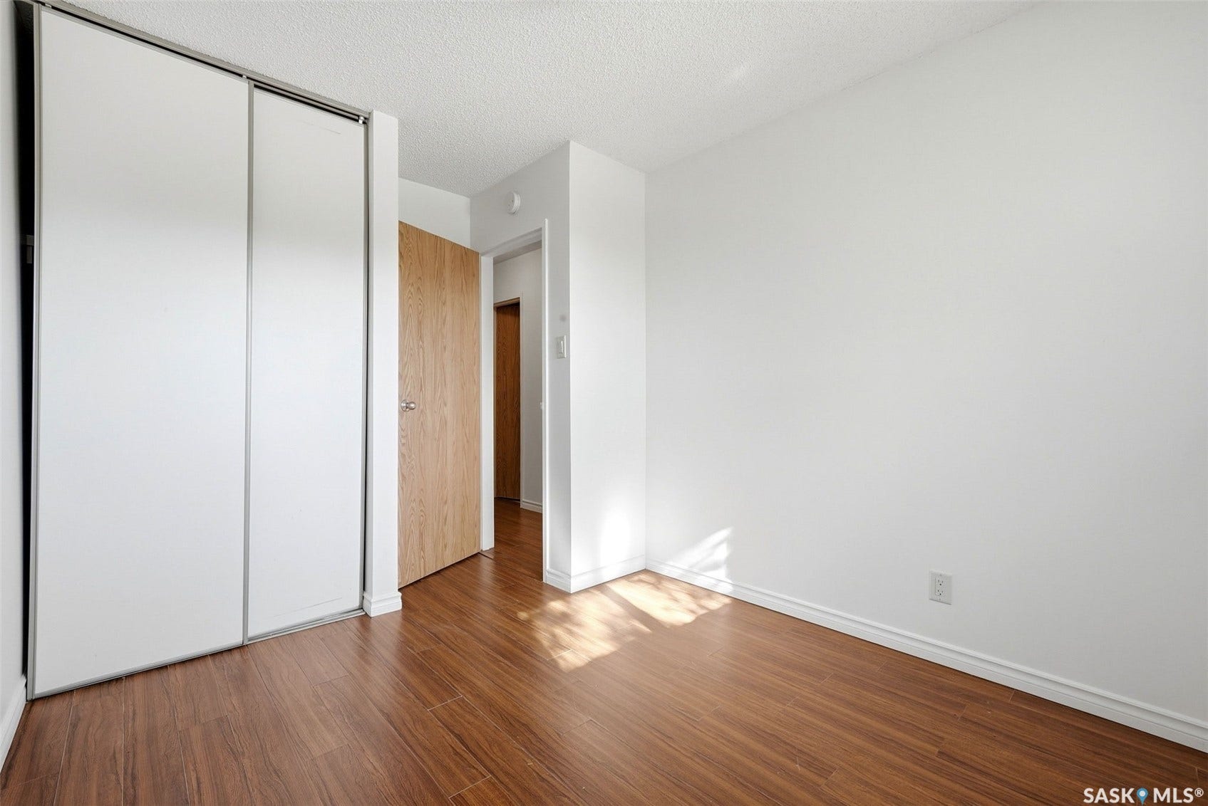 Wood-finish flooring, white walls, white sliding closet doors, and a wood-finish interior door