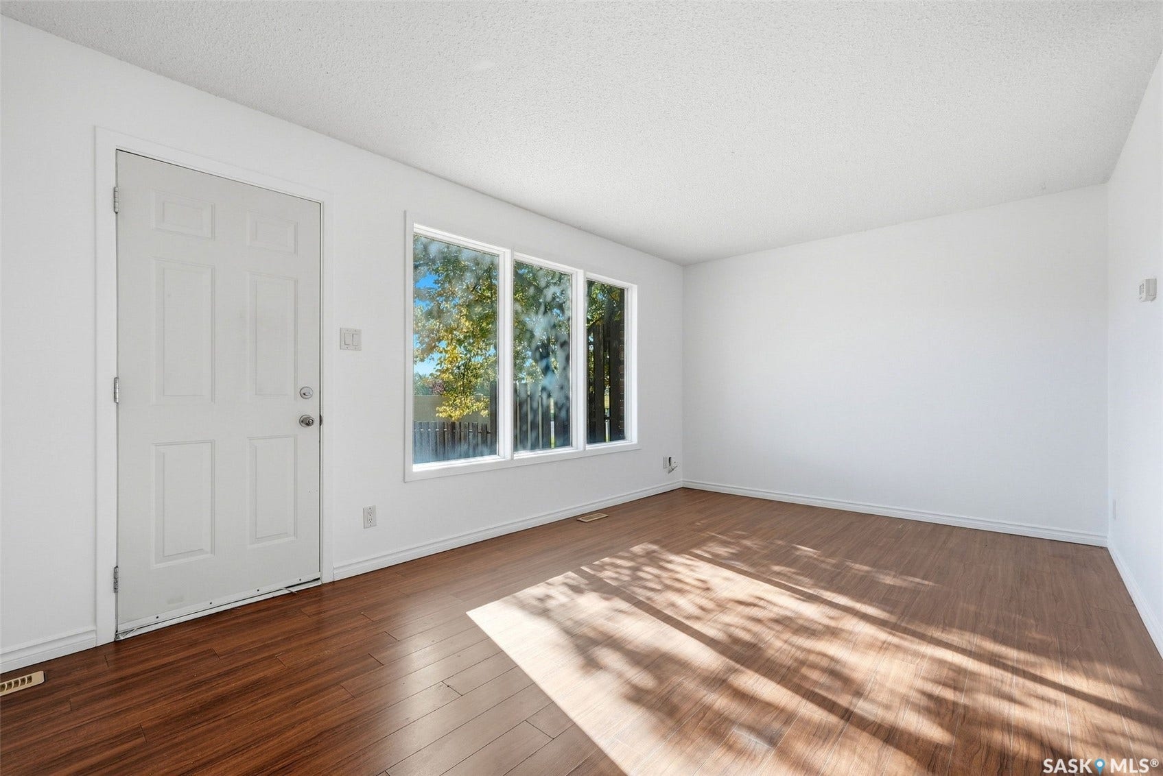 Expansive room with wood-finish flooring, white walls, and a large multi-pane window
