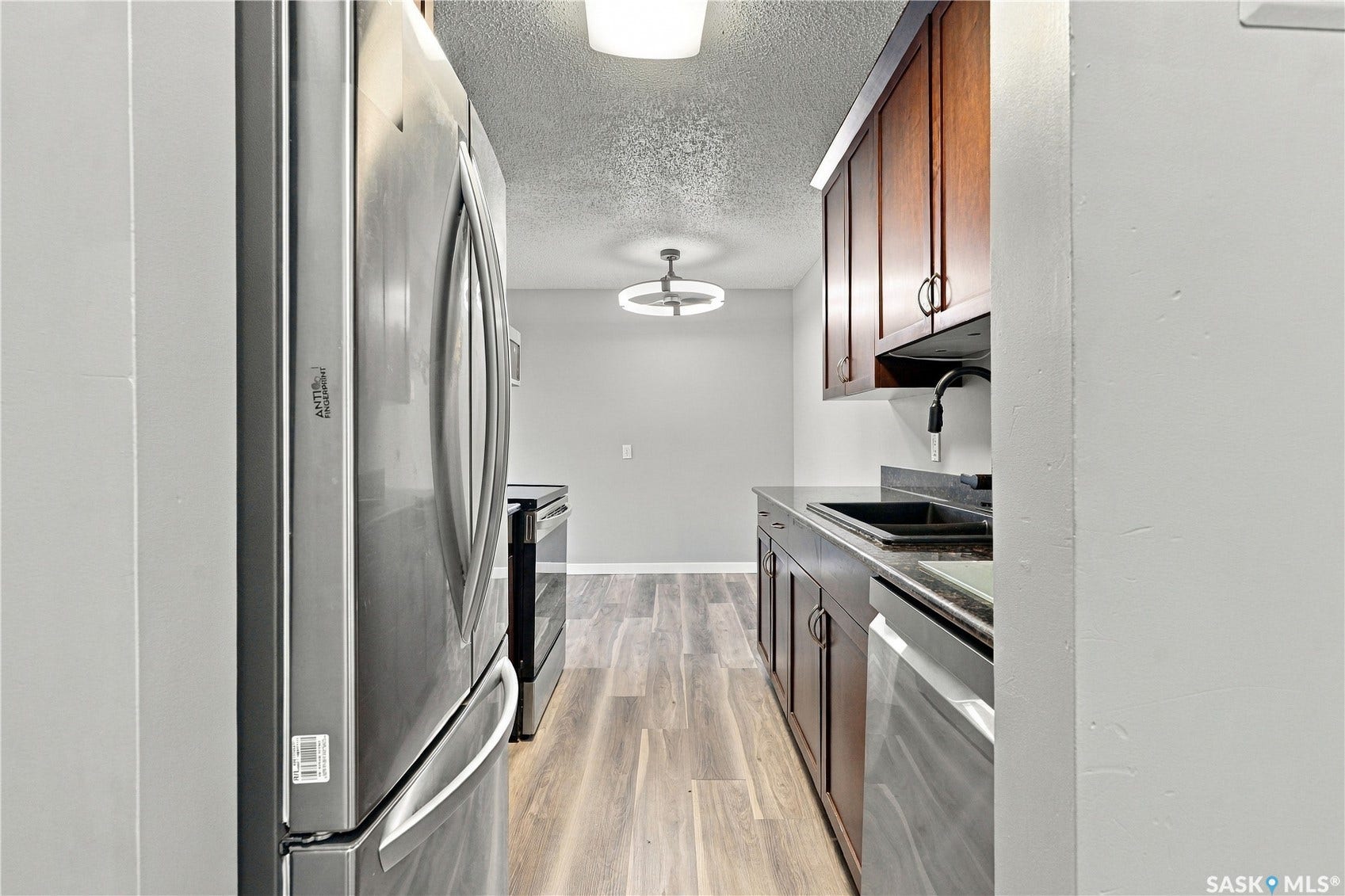Galley kitchen featuring stainless steel appliances, wood-finish flooring, dark countertops, and wood cabinetry