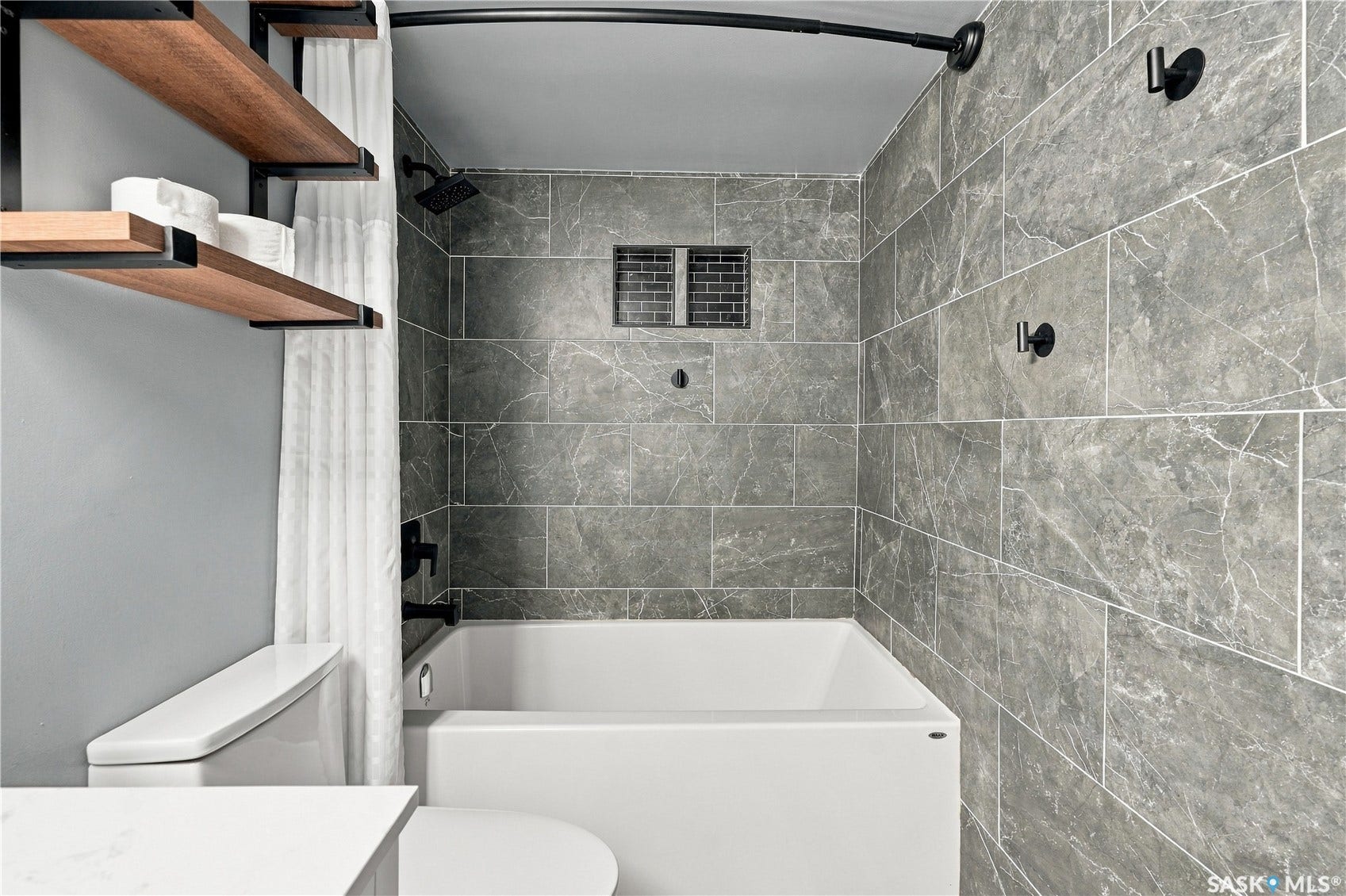 Bathtub with full-height large format tile surround, recessed tiled niche, and matte black fixtures