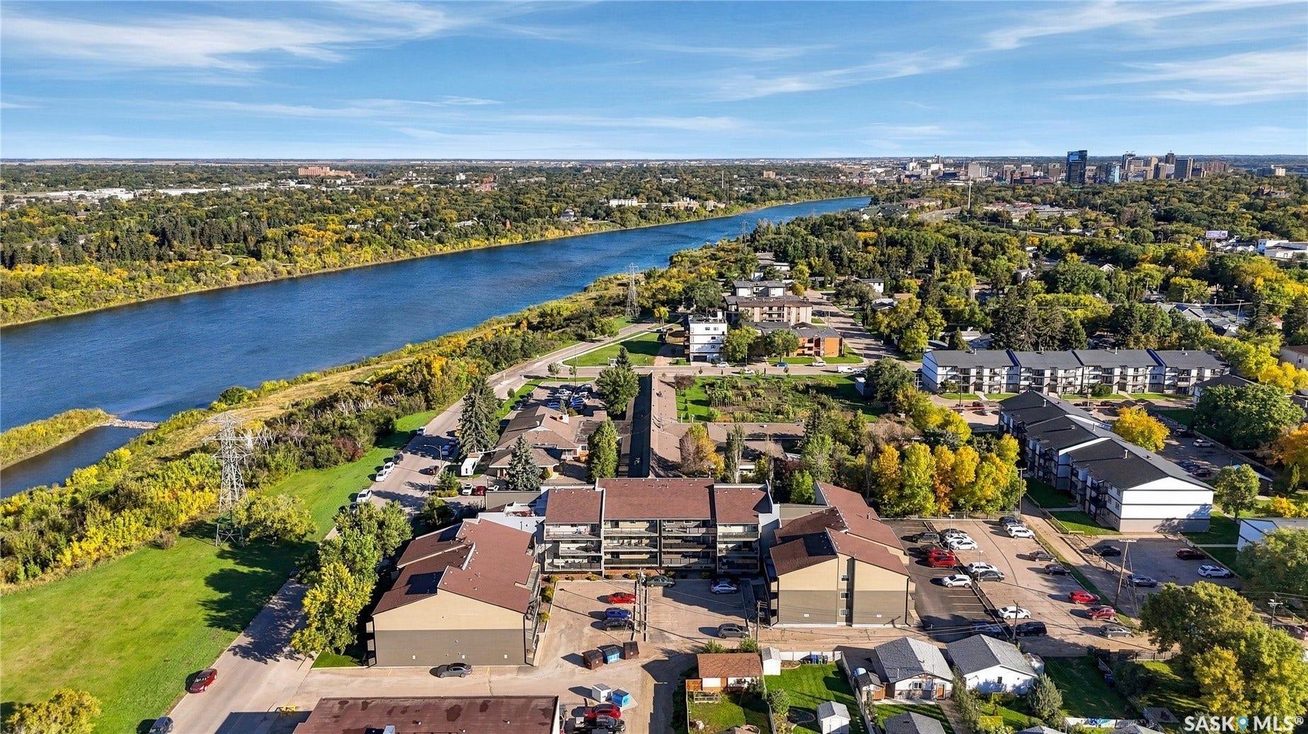 Riverfront community setting with multiple residential buildings, lush green spaces, and mature trees