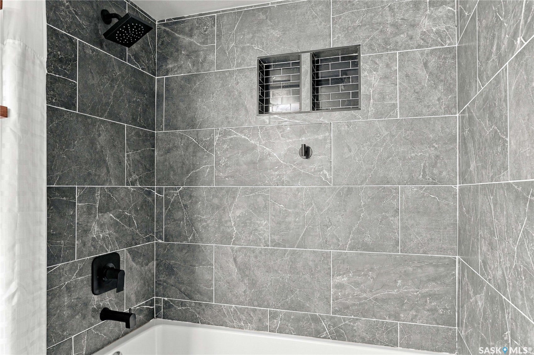 Bathtub with matte black fixtures, recessed shower niche with subway tile, and large format wall tiling