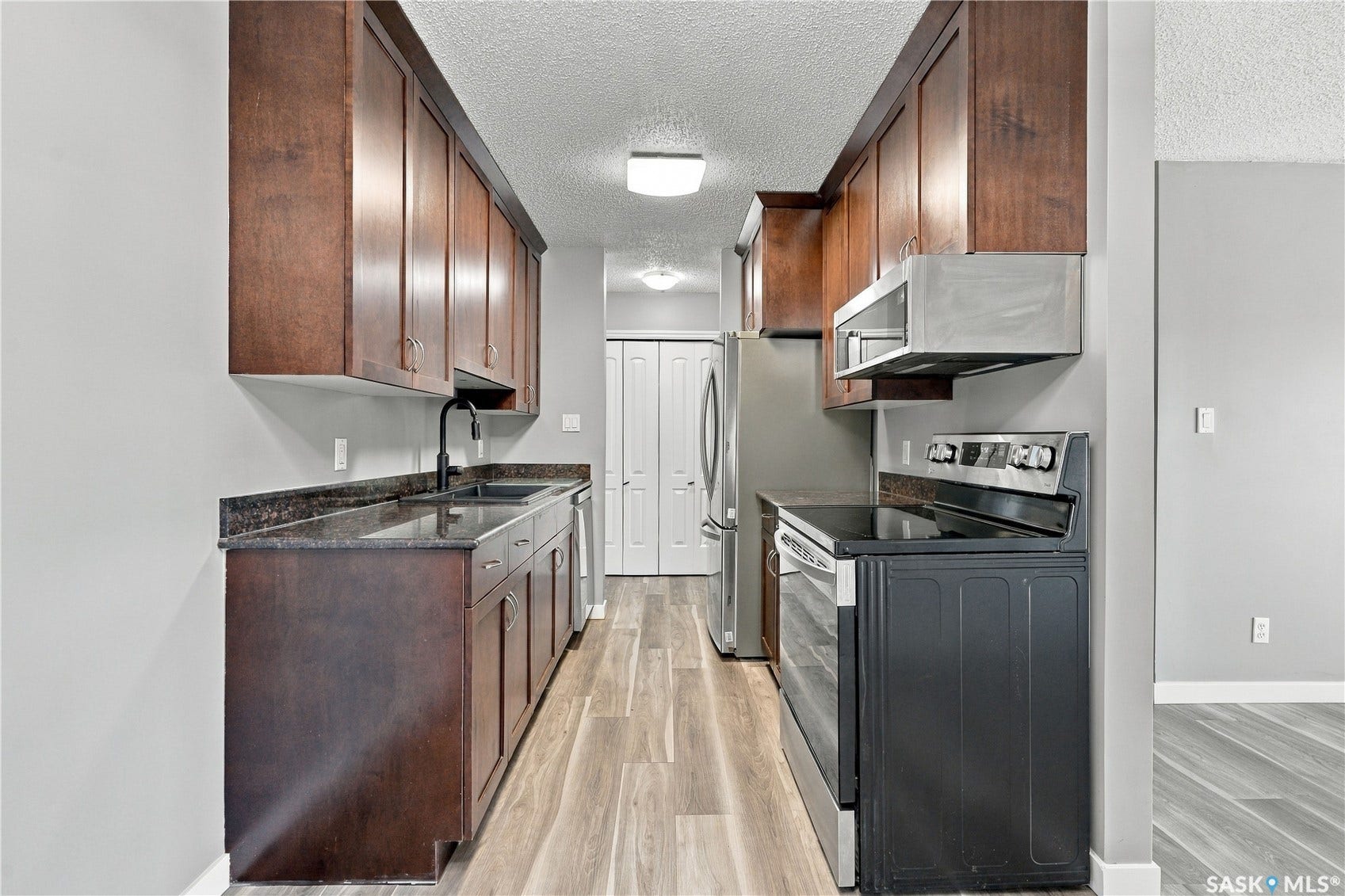 Galley kitchen featuring wood-finish cabinetry, dark countertops, black faucet, and stainless steel appliances