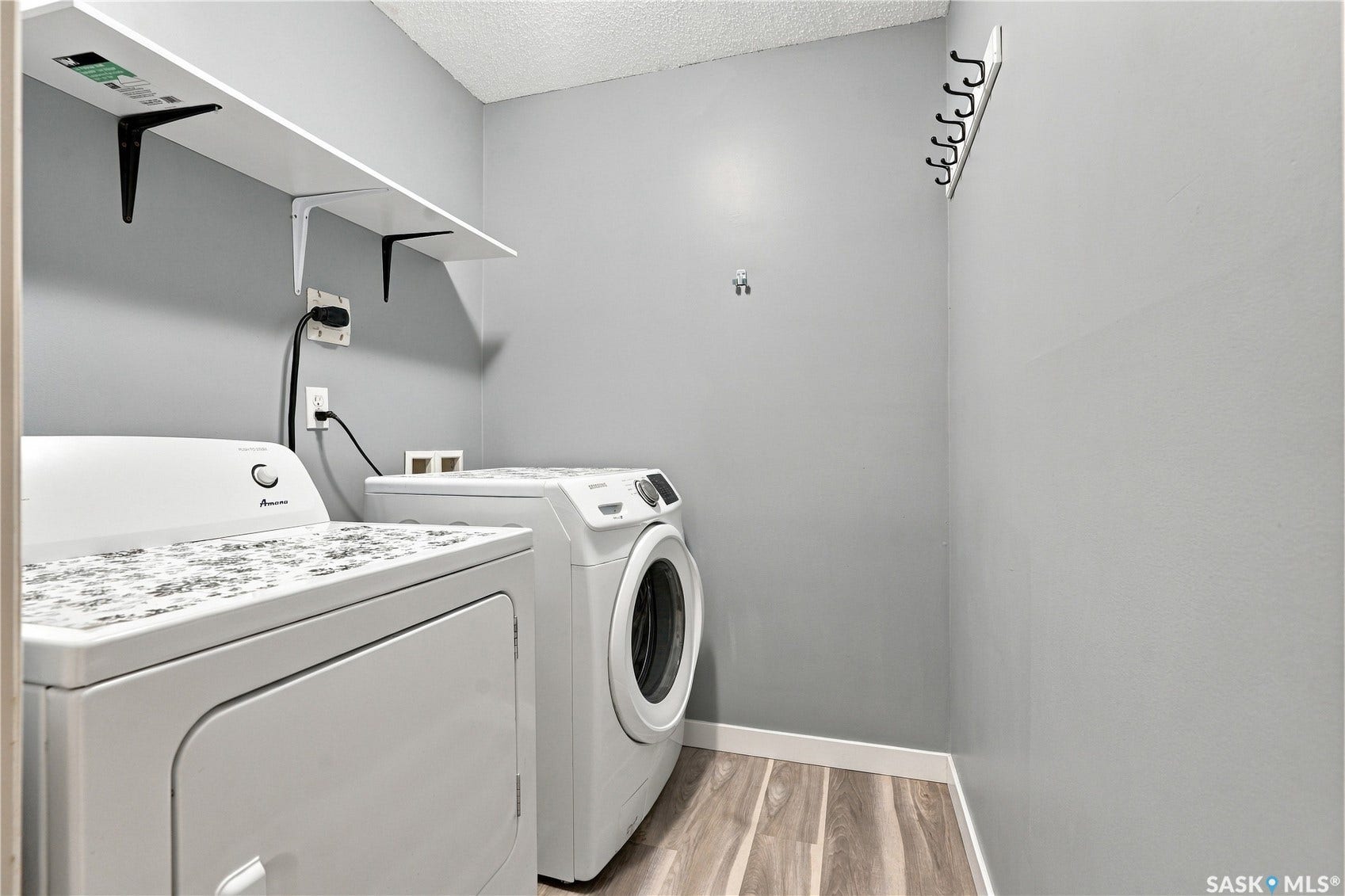 Laundry area featuring wood-finish flooring, wall-mounted shelving, and a wall-mounted coat rack