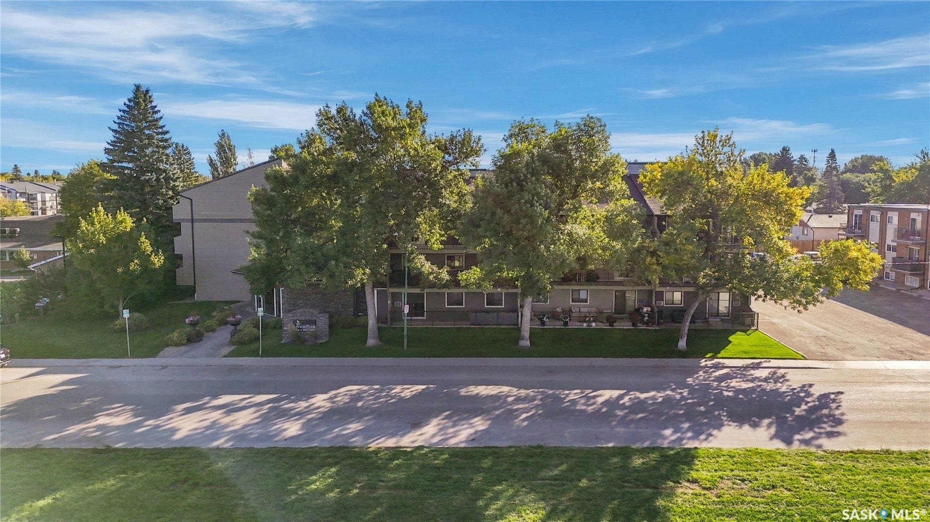 Multi-story residential building with stone accents, mature trees, and a paved walkway
