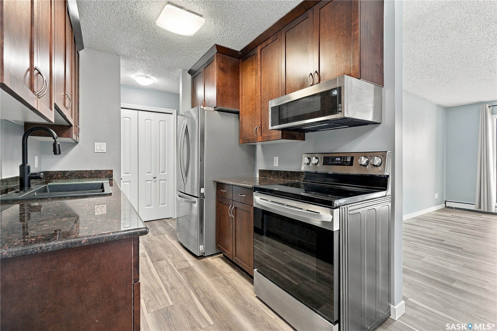 Modern kitchen featuring wood-finish cabinetry, dark stone countertops, and stainless steel appliances