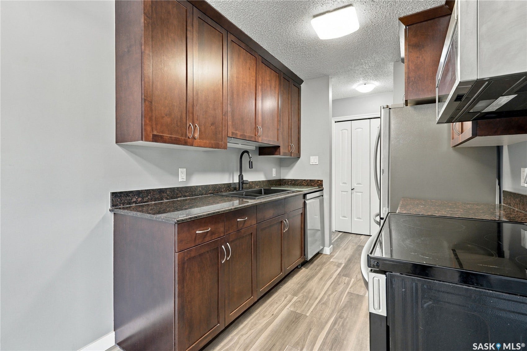 Kitchen featuring wood-finish cabinetry, dark countertops, a stainless steel refrigerator, and wood-finish flooring