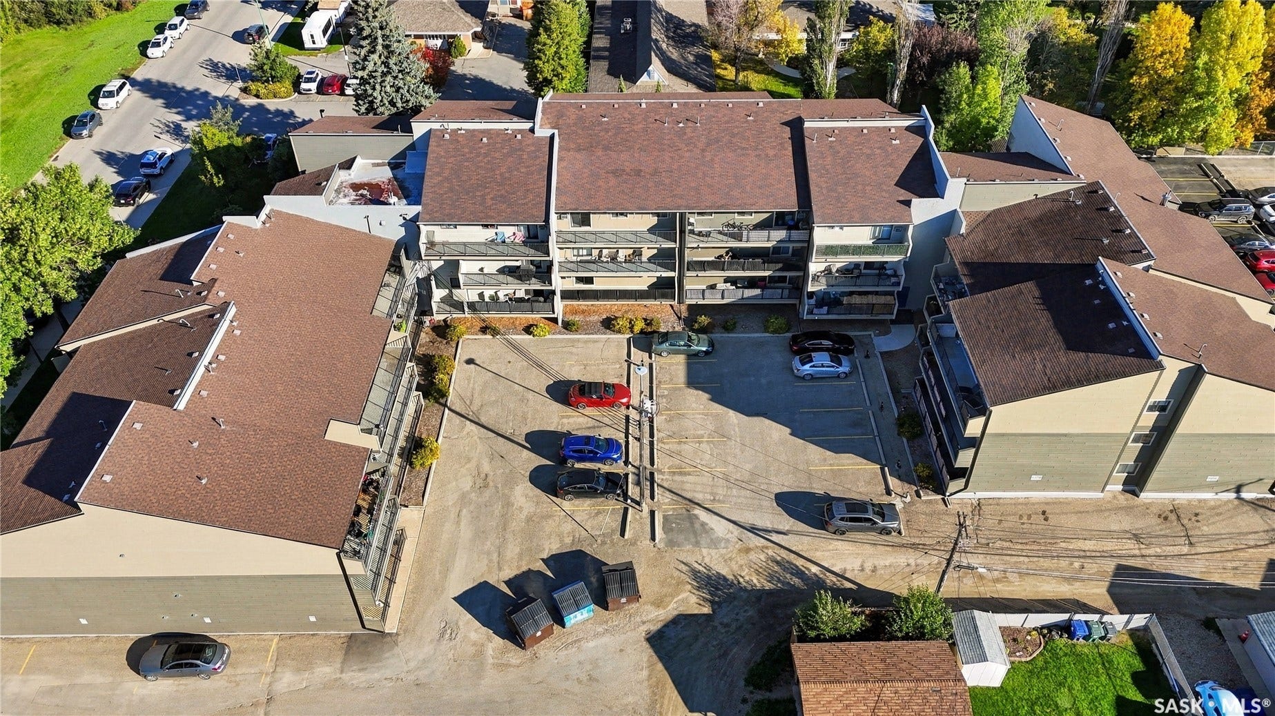 Multi-unit residential property featuring a large asphalt parking area, multiple levels of private balconies with glass railings, and a shingle roof