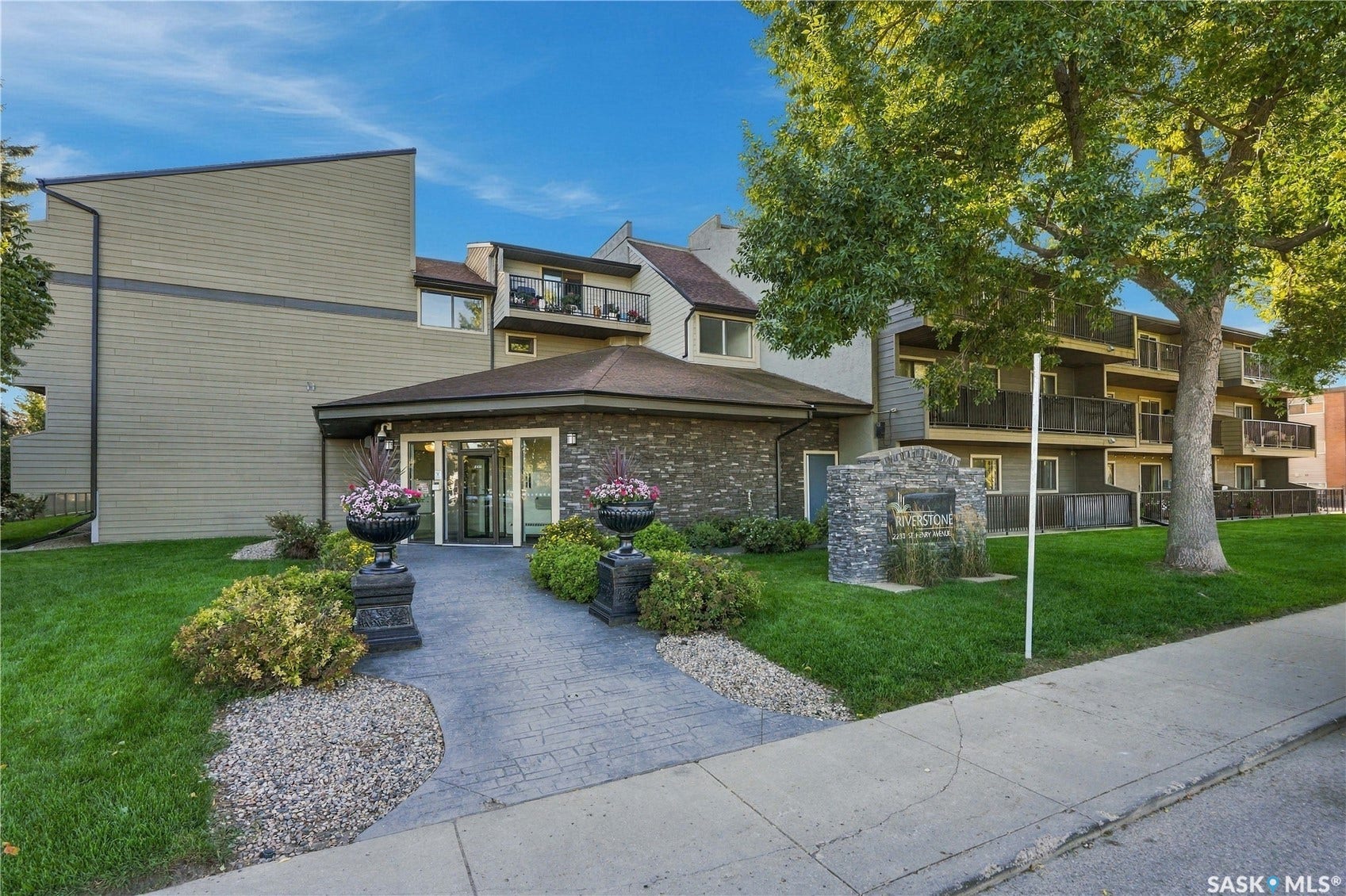 Stone veneer and horizontal siding exterior, stamped concrete pathway, mature landscaping, and balconies