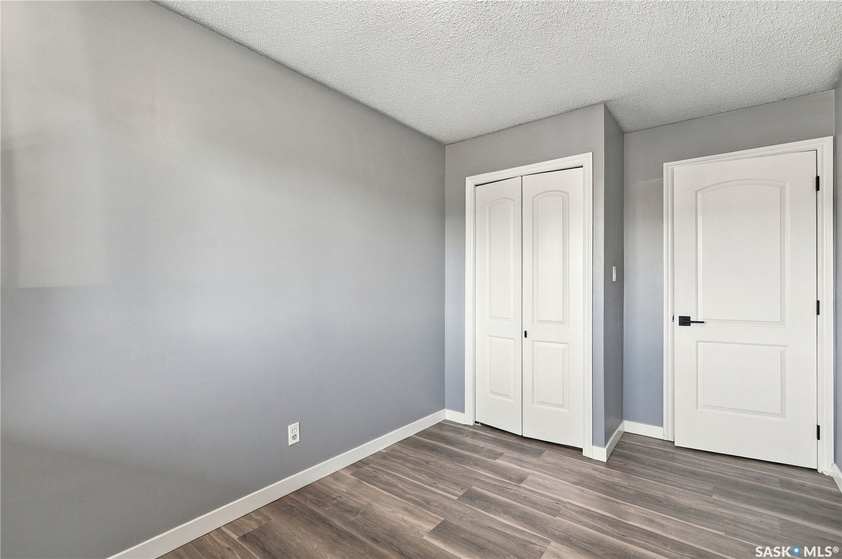 Wood-finish flooring, white trim, textured ceiling, and a white interior door with matte black hardware