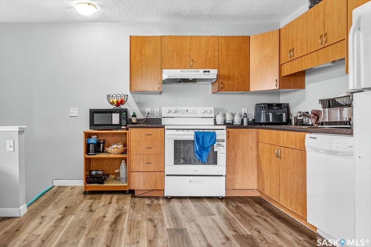 5051 James Hill Road, #107, Regina SK S4W 0B9 Wood-finish flooring, light wood cabinetry, white appliances, and a dark countertop