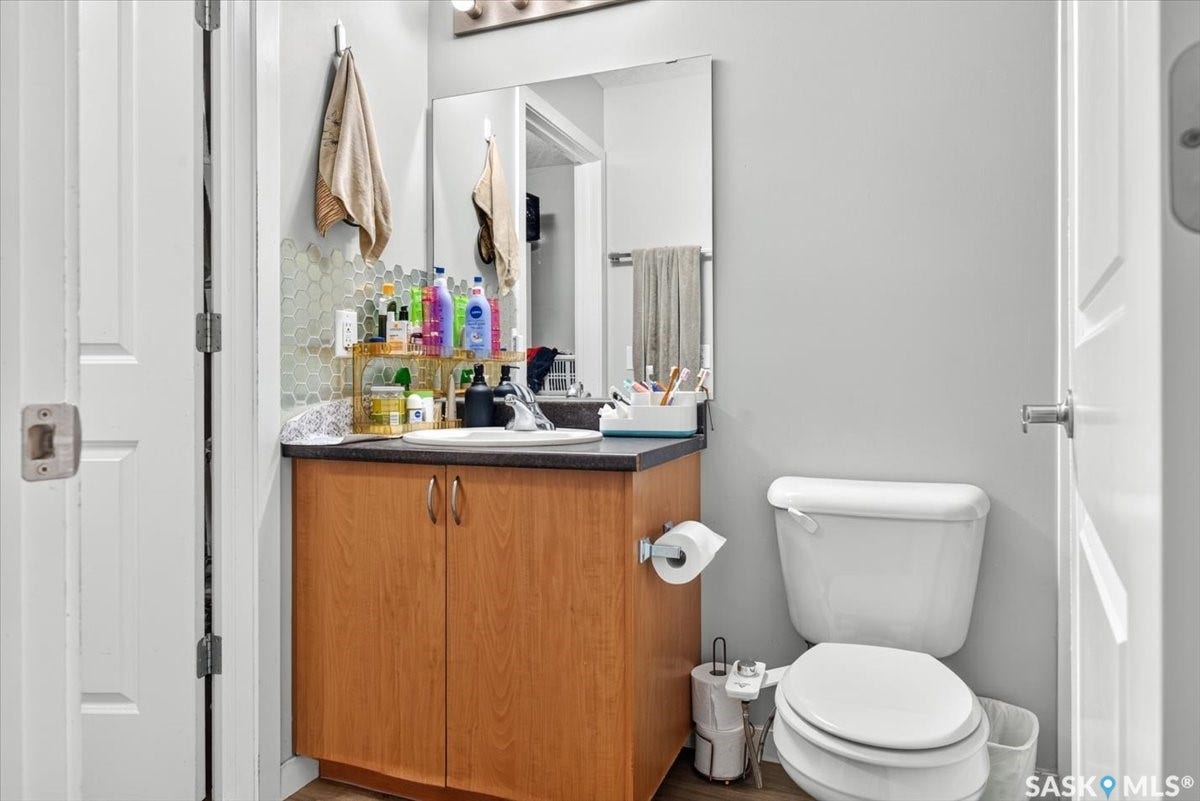 5051 James Hill Road, #107, Regina SK S4W 0B9 Wood-finish vanity with an integrated sink, dark countertop, honeycomb tile backsplash, and overhead vanity lighting