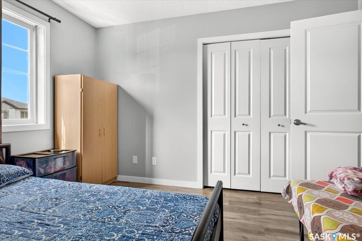 5051 James Hill Road, #107, Regina SK S4W 0B9 Light gray walls with a white trim, wood-finish flooring, a white window, and bi-fold closet doors