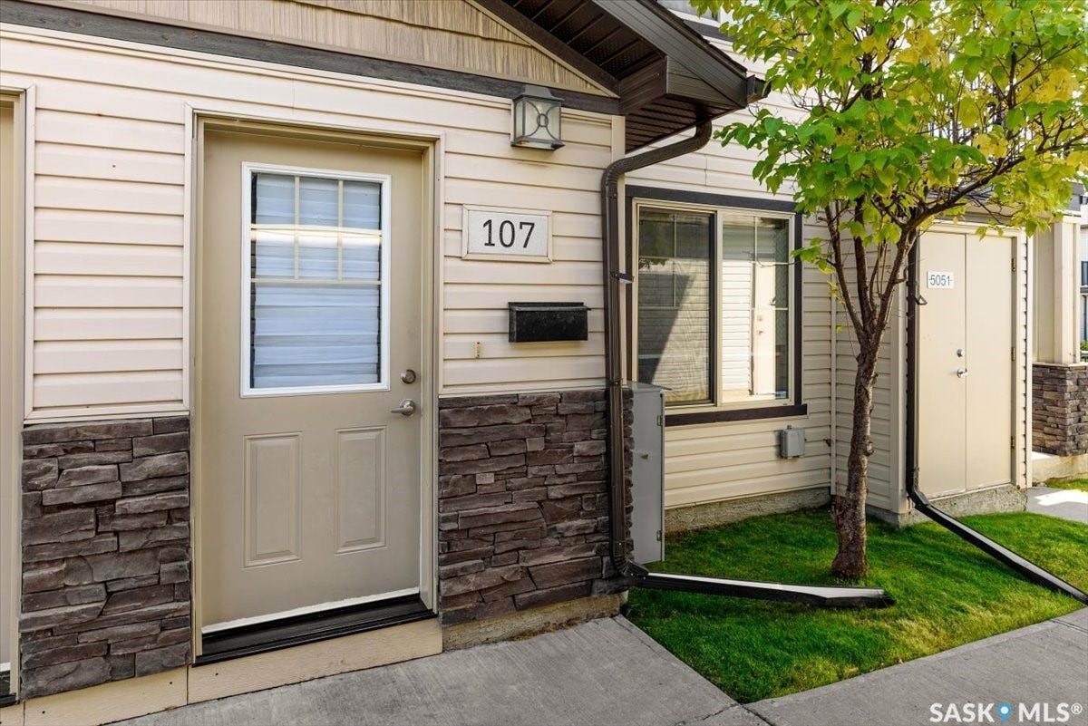 5051 James Hill Road, #107, Regina SK S4W 0B9 Entry door with upper window panes, stone veneer facade detailing, horizontal siding, and an exterior light fixture