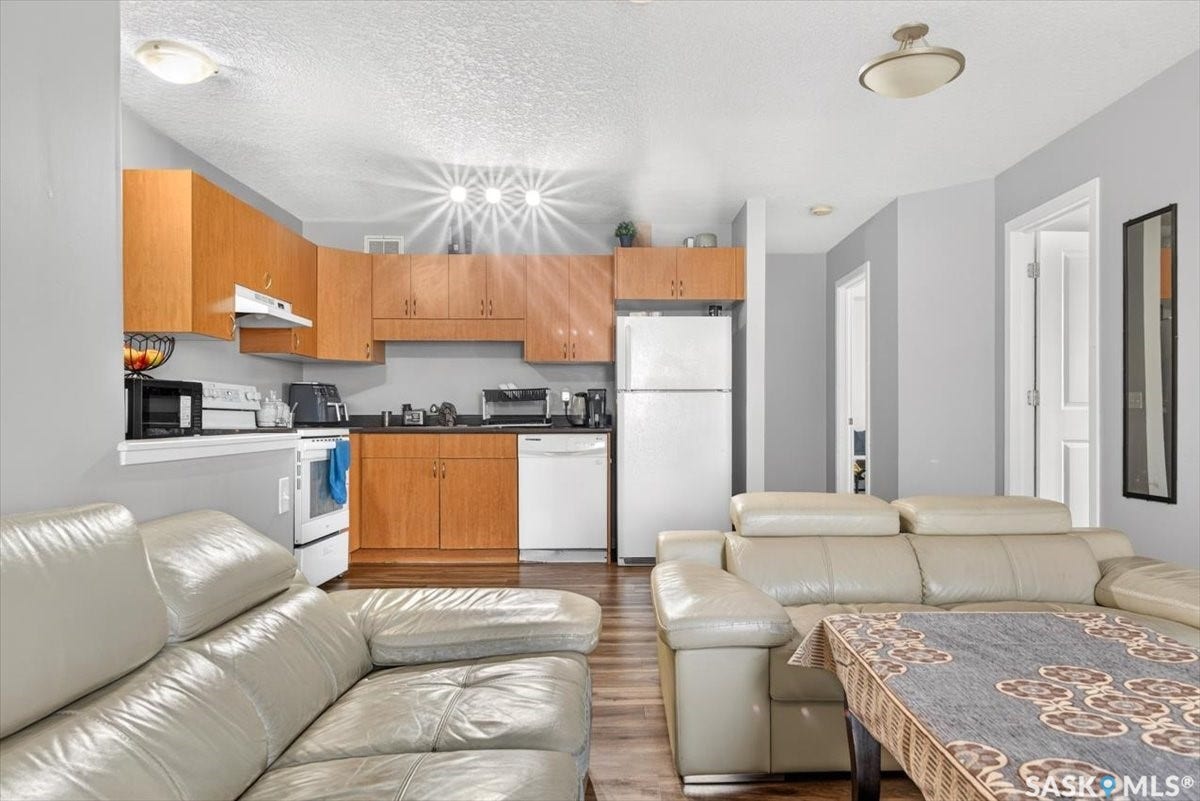 5051 James Hill Road, #107, Regina SK S4W 0B9 Kitchen featuring wood-finish cabinetry, black countertops, and white appliances
