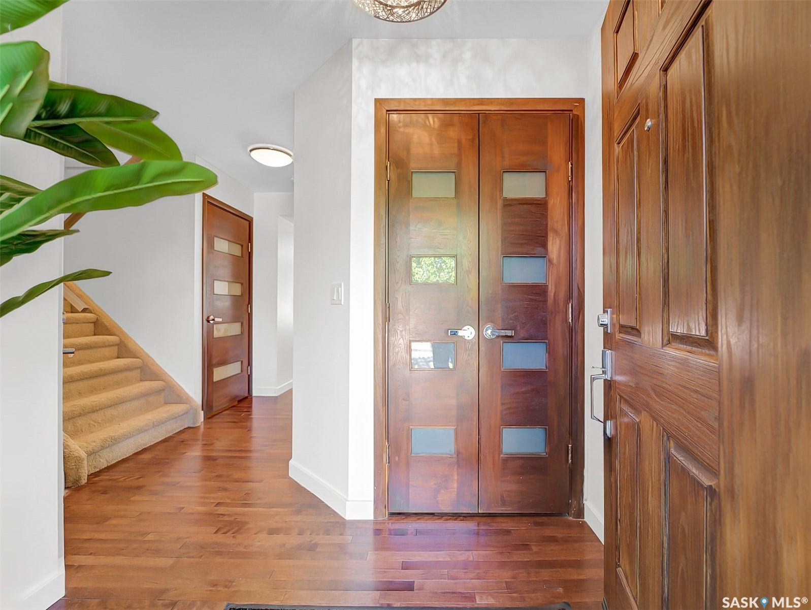 Solid wood entry door with polished hardware, hardwood flooring, dual wood doors with frosted glass panels, carpeted staircase, and recessed lighting
