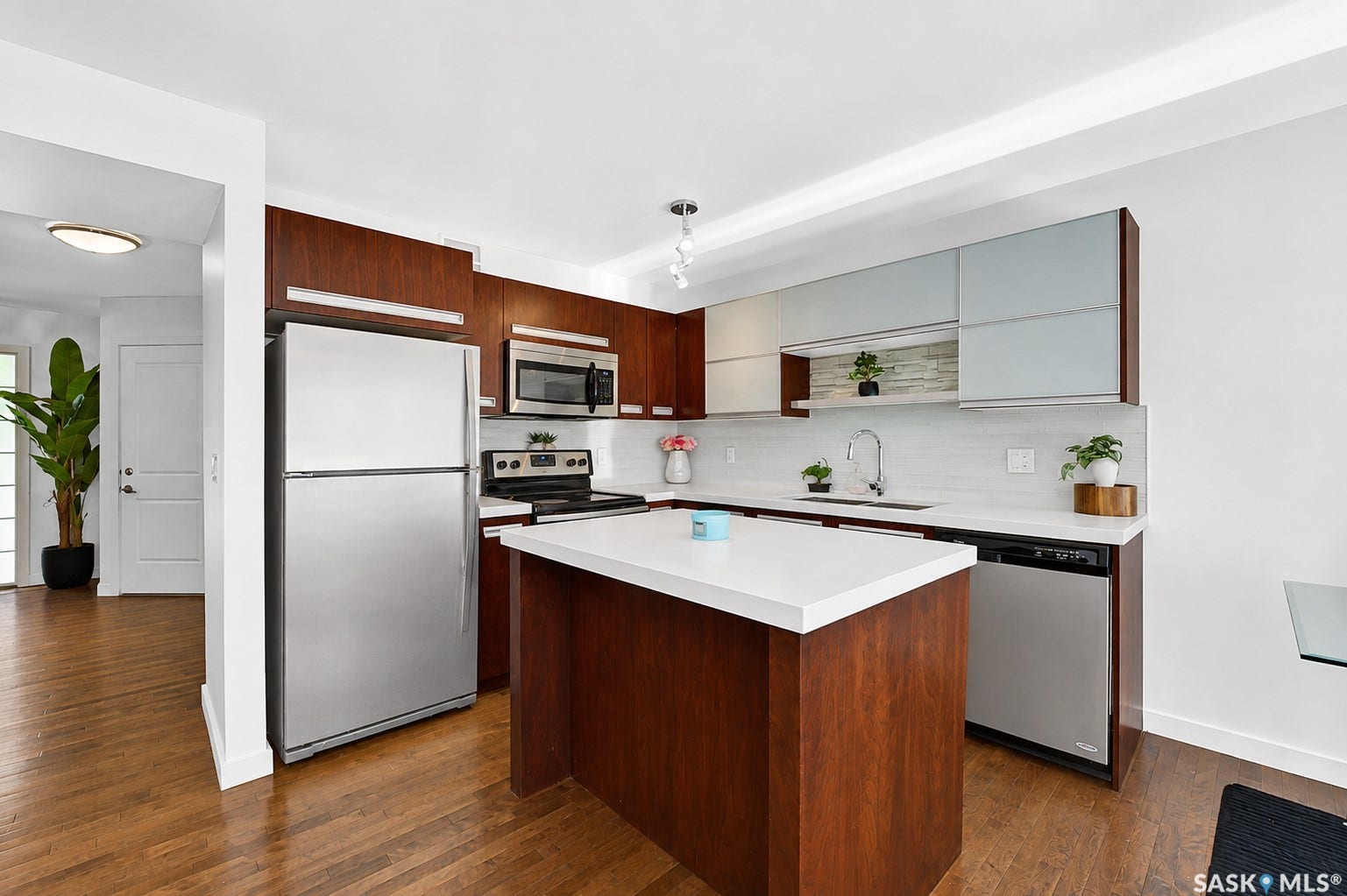 Contemporary kitchen featuring stainless steel appliances, a center island with a white countertop, wood-finish cabinetry, and a tile backsplash