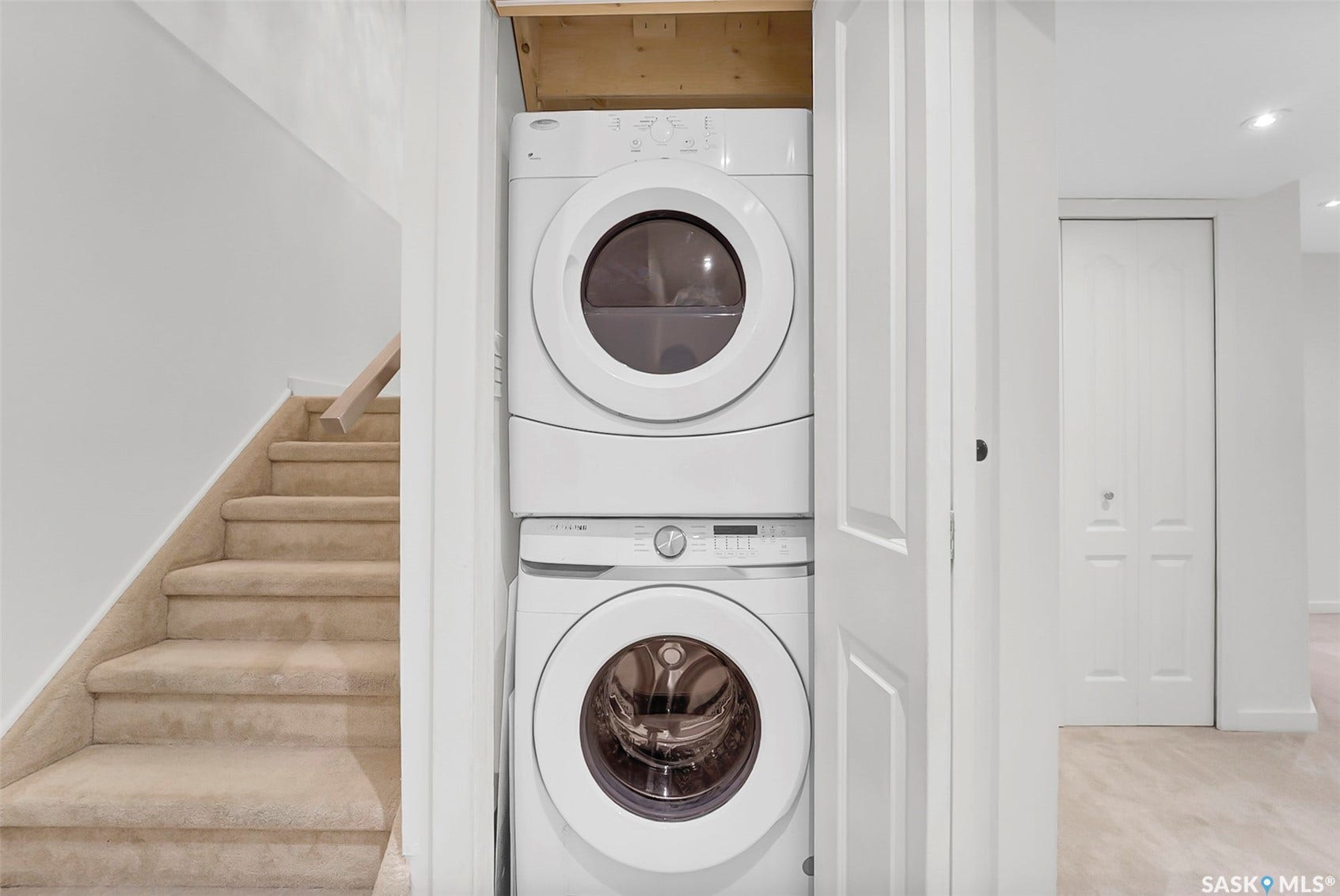 Stackable washer and dryer unit, carpeted staircase with wood handrail, and interior paneled doors