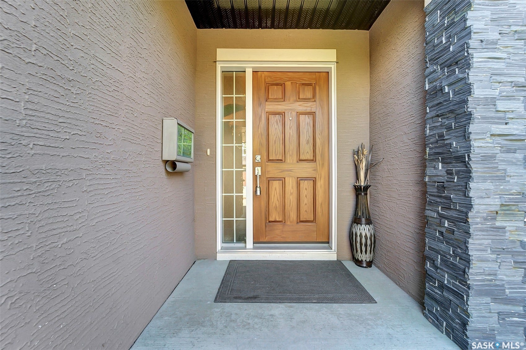 Wood-panel entry door with sidelight, textured stucco wall, and stacked stone accent