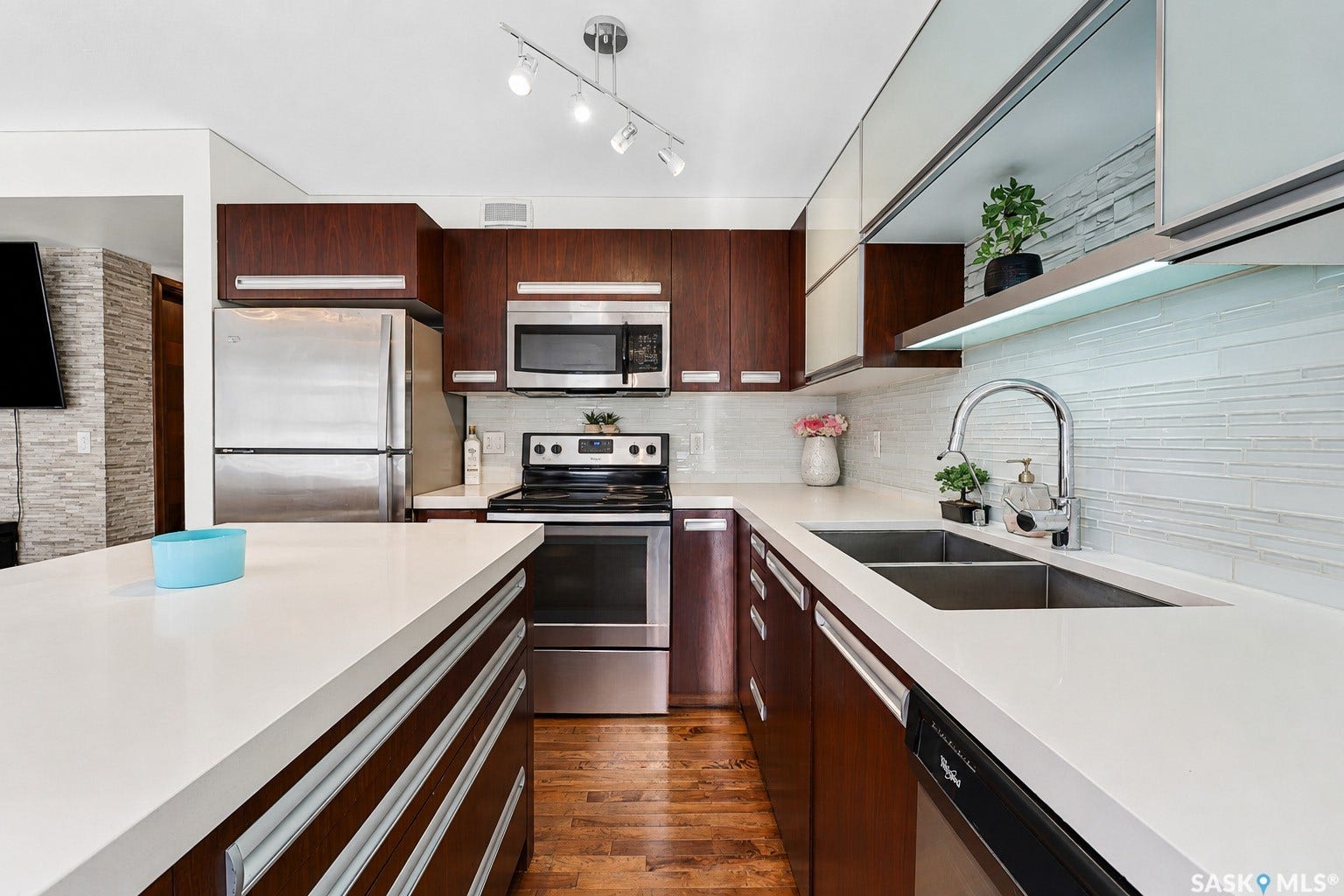 Modern kitchen featuring wood-finish cabinetry, stainless steel appliances, white countertops, a dual basin sink with a gooseneck faucet, and a horizontally stacked tile backsplash