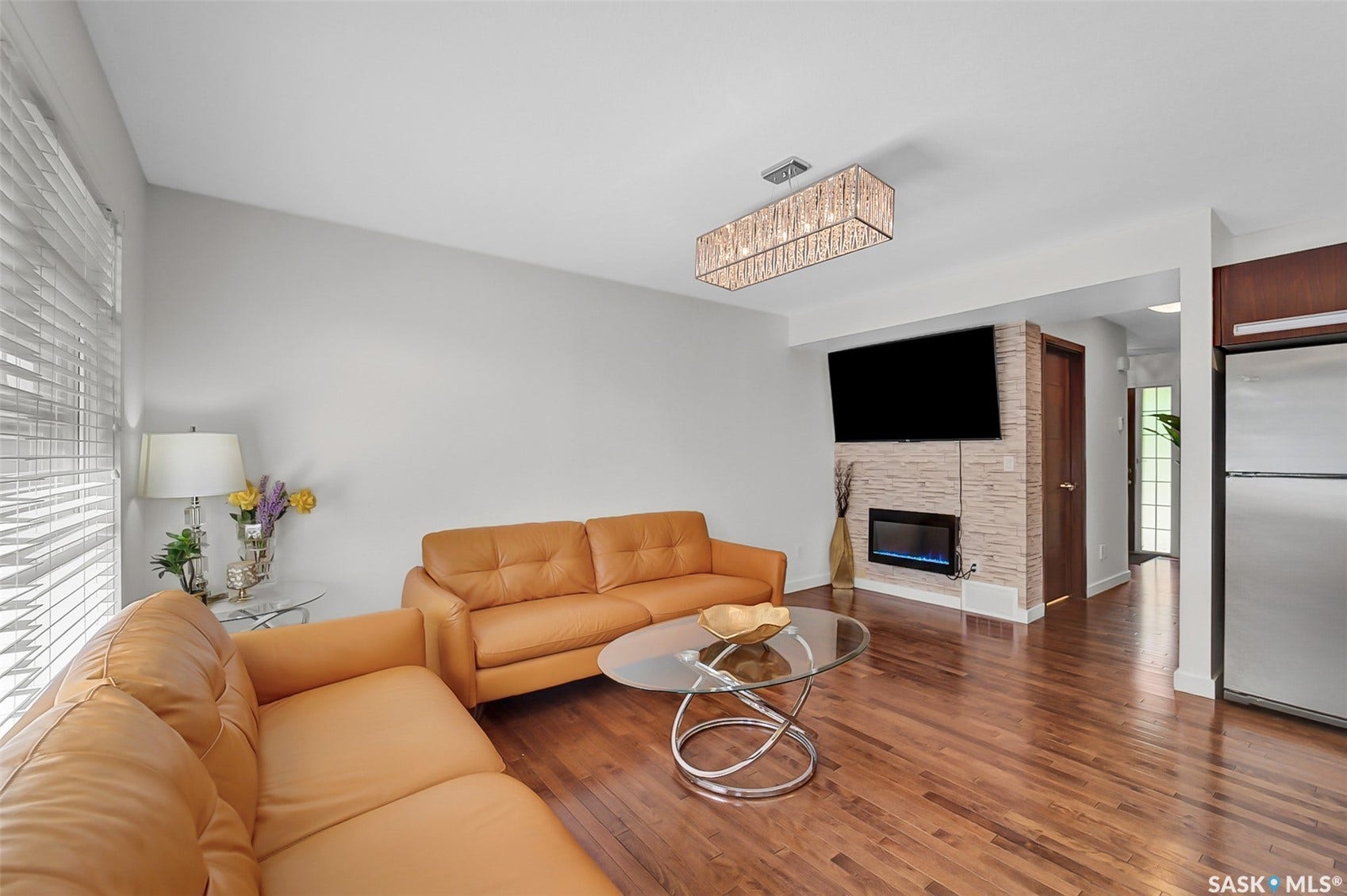 Hardwood flooring, recessed fireplace with stone surround, a rectangular chandelier, and stainless steel appliances