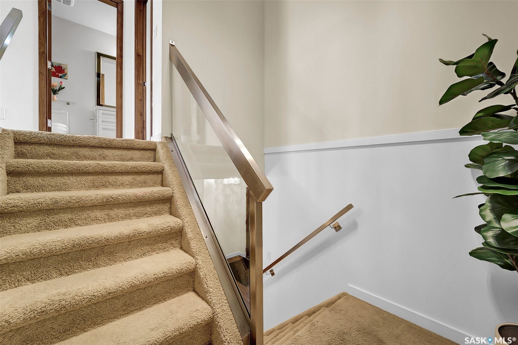 Carpeted staircase featuring a glass and metal railing system, wainscoting, and wood-framed doorway