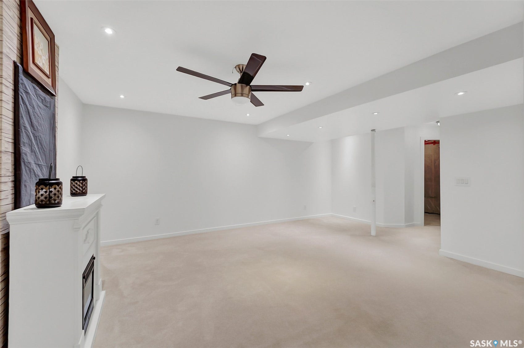 Recessed ceiling lighting, ceiling-mounted fan, plush carpeting, white trim, and a white fireplace mantel