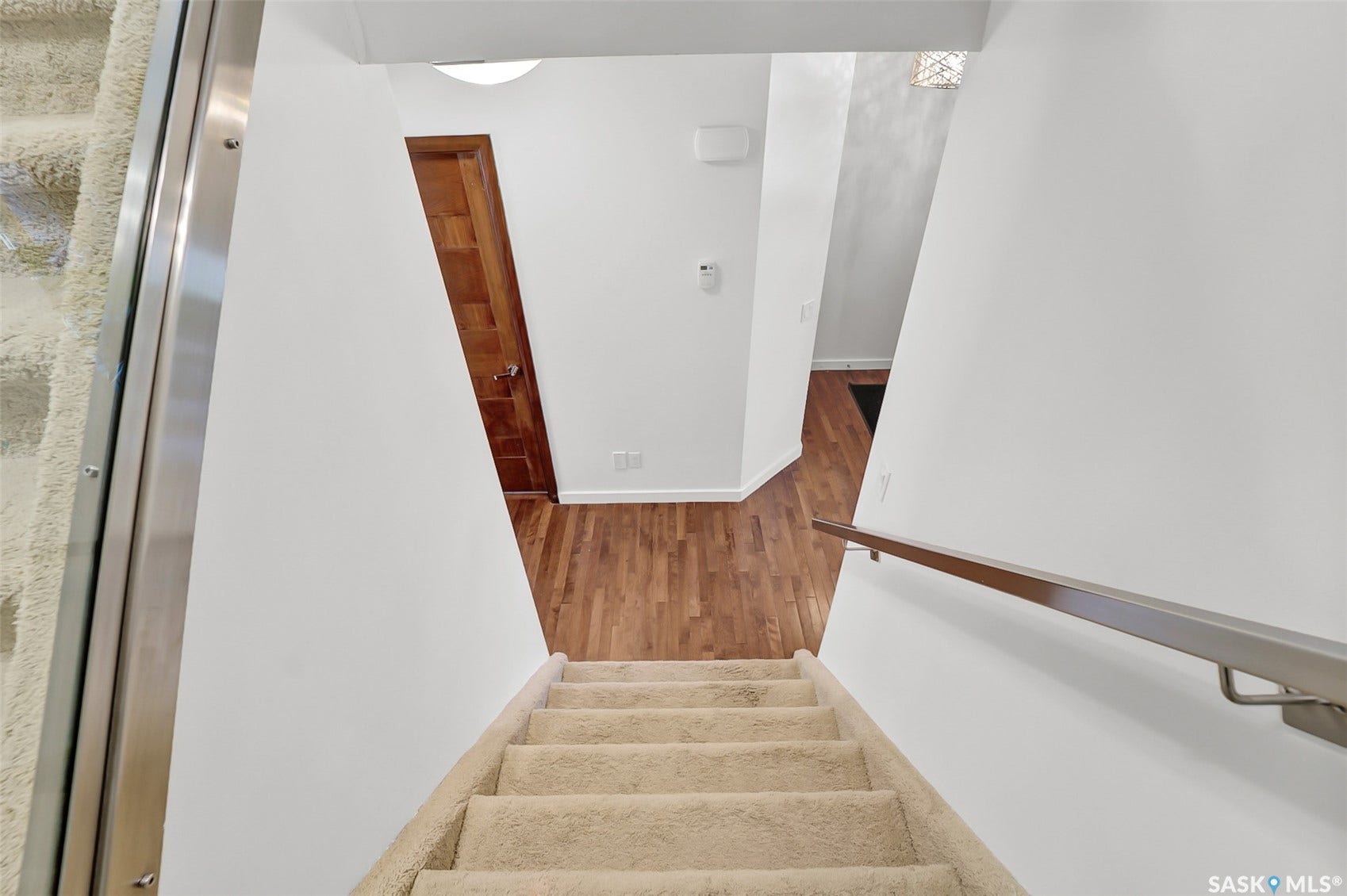 Carpeting on stairs, wood-finish flooring, interior door with panel detailing, modern wall-mounted handrail, contemporary wall-mounted light fixture
