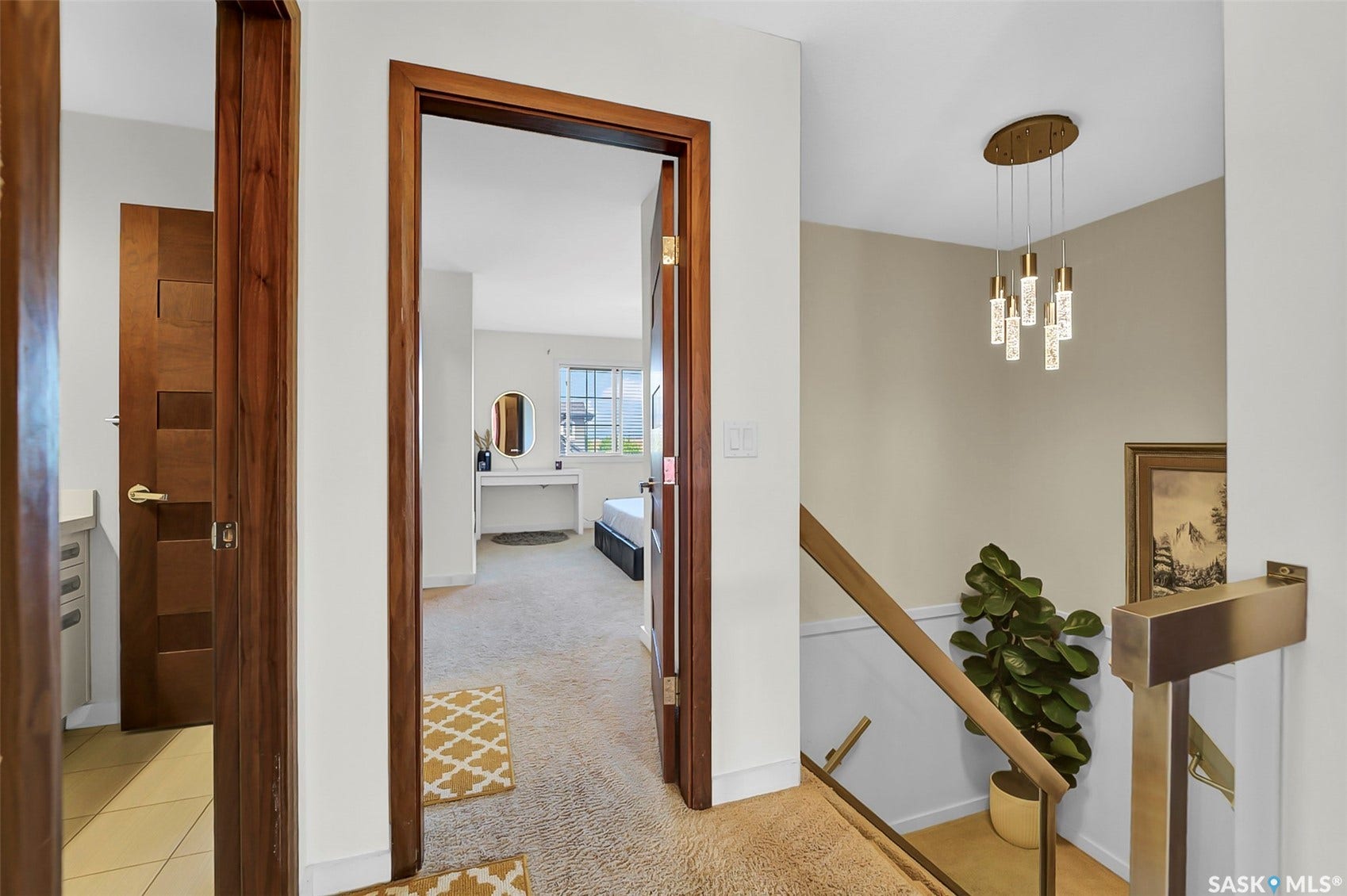 Modern multi-light pendant fixture, staircase with brass railing, wood-finish door frames, and textured carpeting