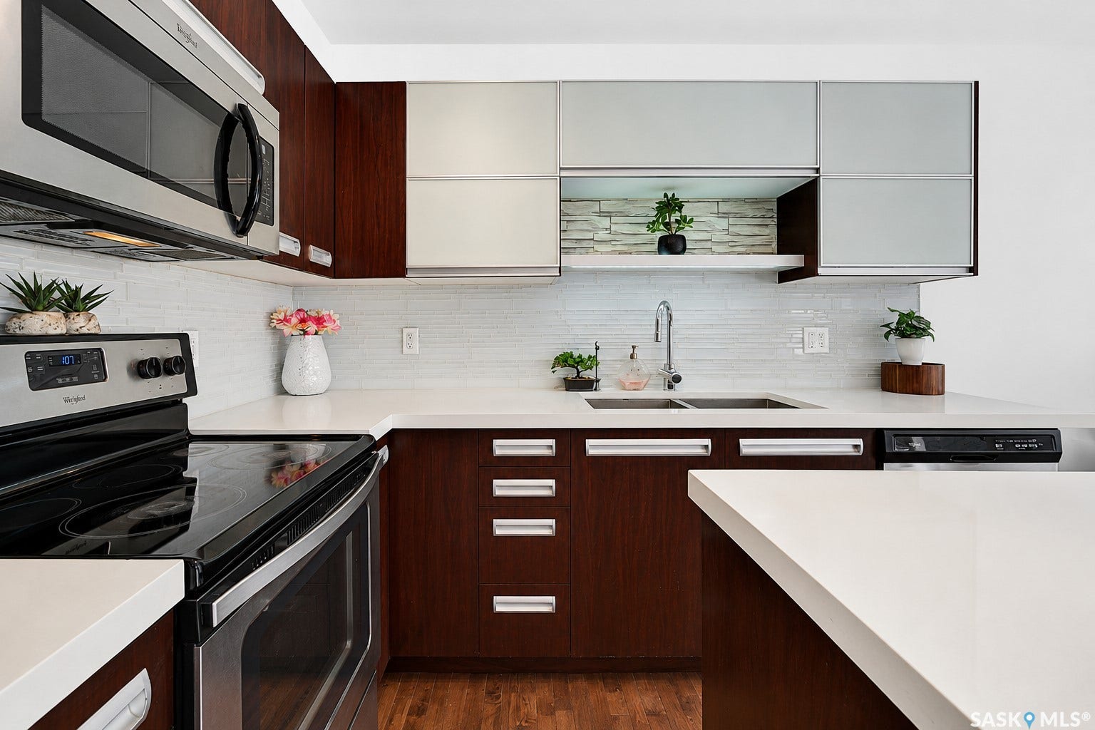 Sleek kitchen featuring wood-finish lower cabinetry, white upper cabinetry, light subway tile backsplash, and a stainless steel appliance suite