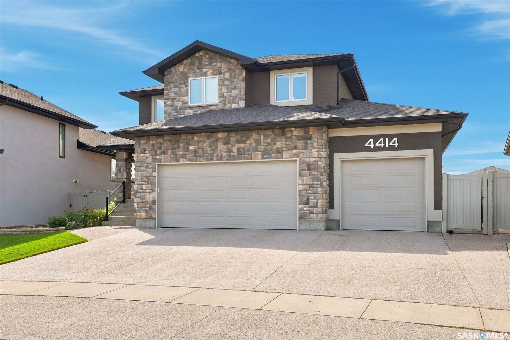 4414 Sandpiper Crescent E, Regina SK S4V 1N3 Two-story residence featuring a stone and stucco exterior, dual garage doors, a concrete driveway, and a fenced side yard