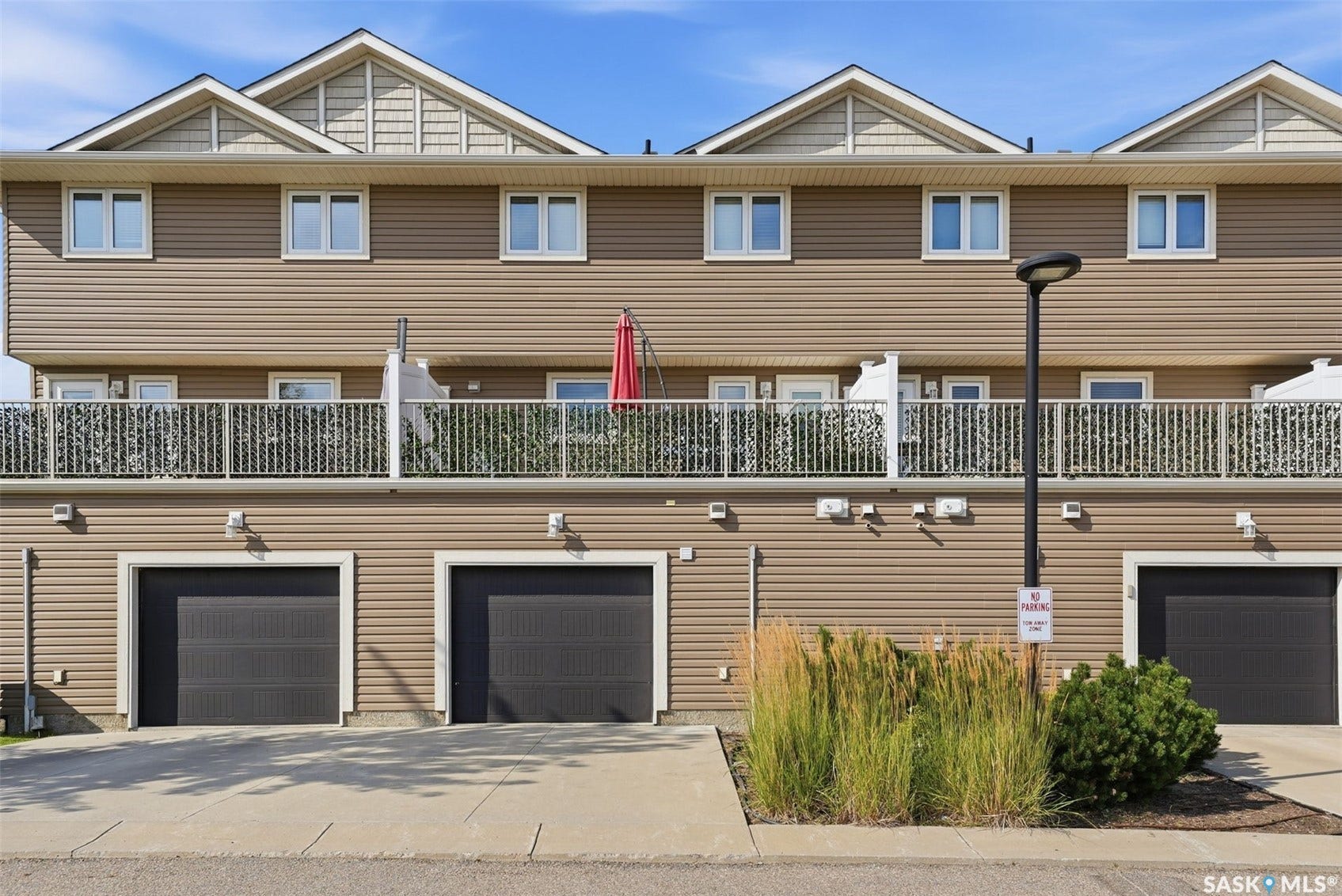 Multi-level exterior with horizontal siding, multiple balconies with white railings, and three ground-level garage doors