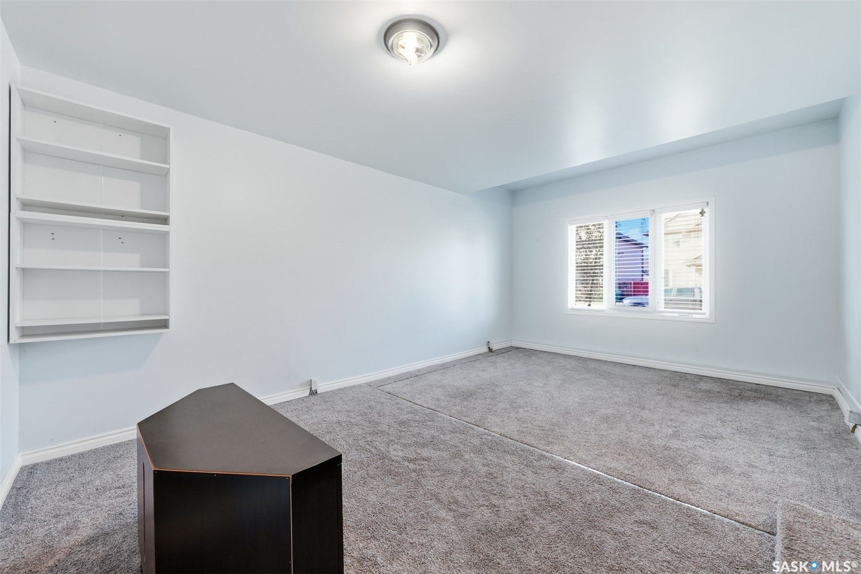 Recessed ceiling light fixture, built-in shelving, window with horizontal blinds, and gray carpeting