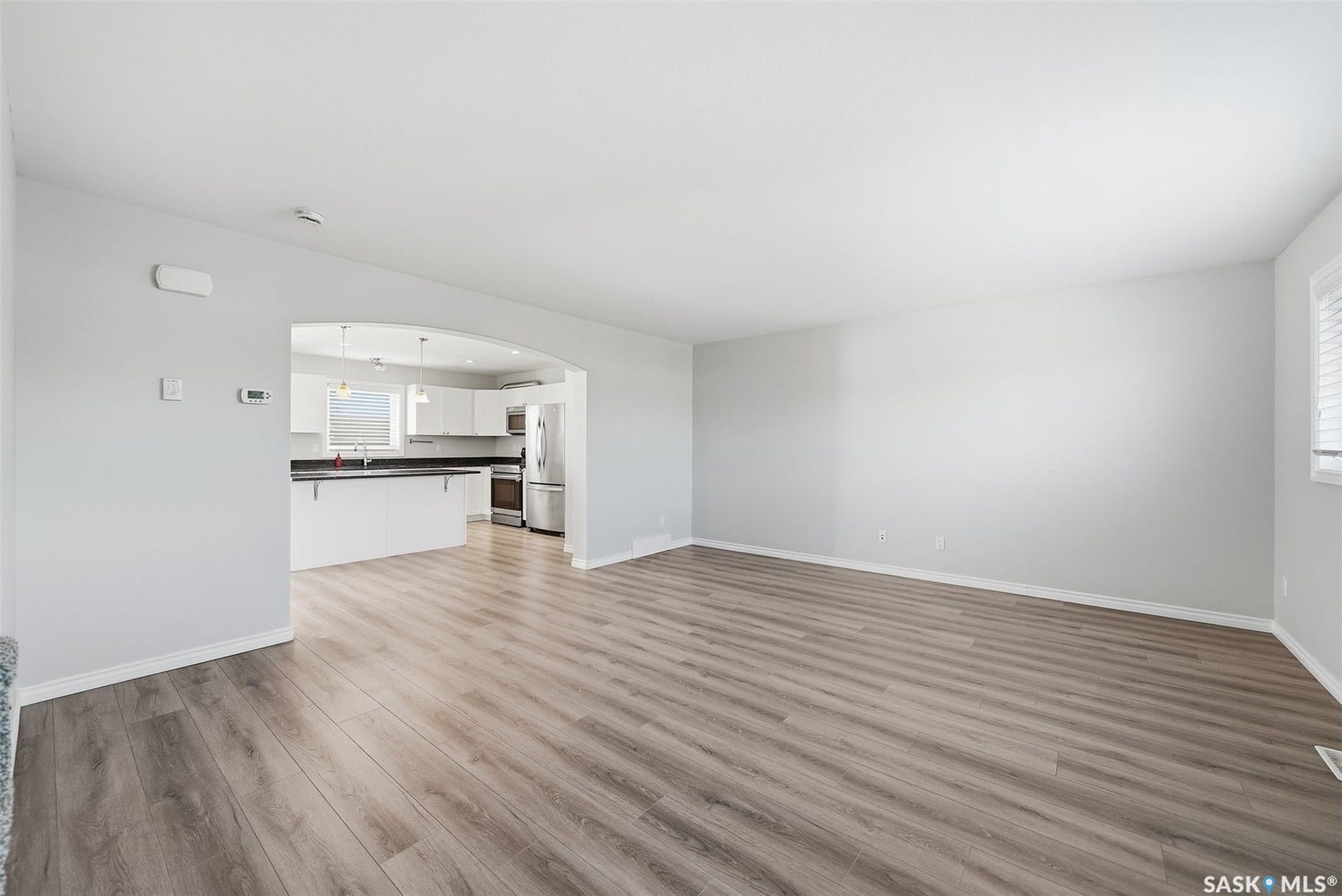 Open-concept living space with wood-finish flooring, white walls, and an arched entryway