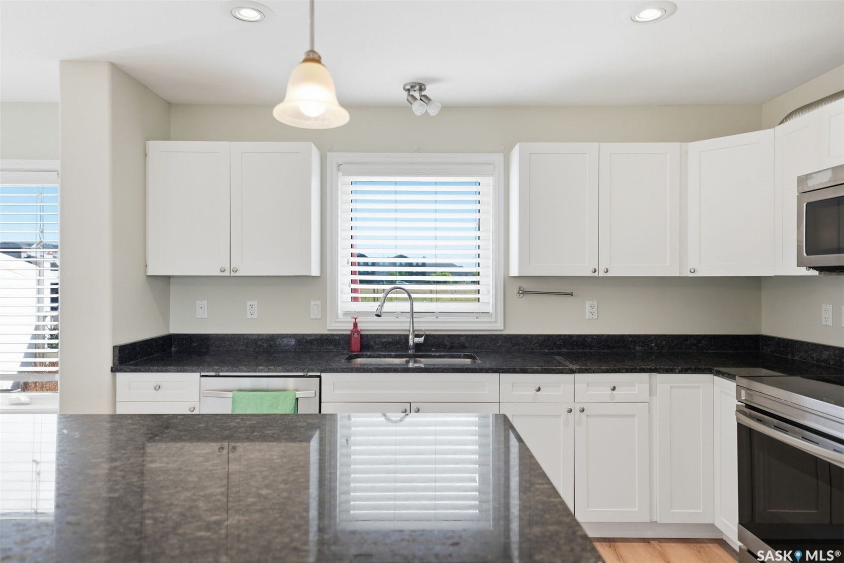 White cabinetry, dark stone countertops, stainless steel appliances, recessed lighting, and a pendant light fixture