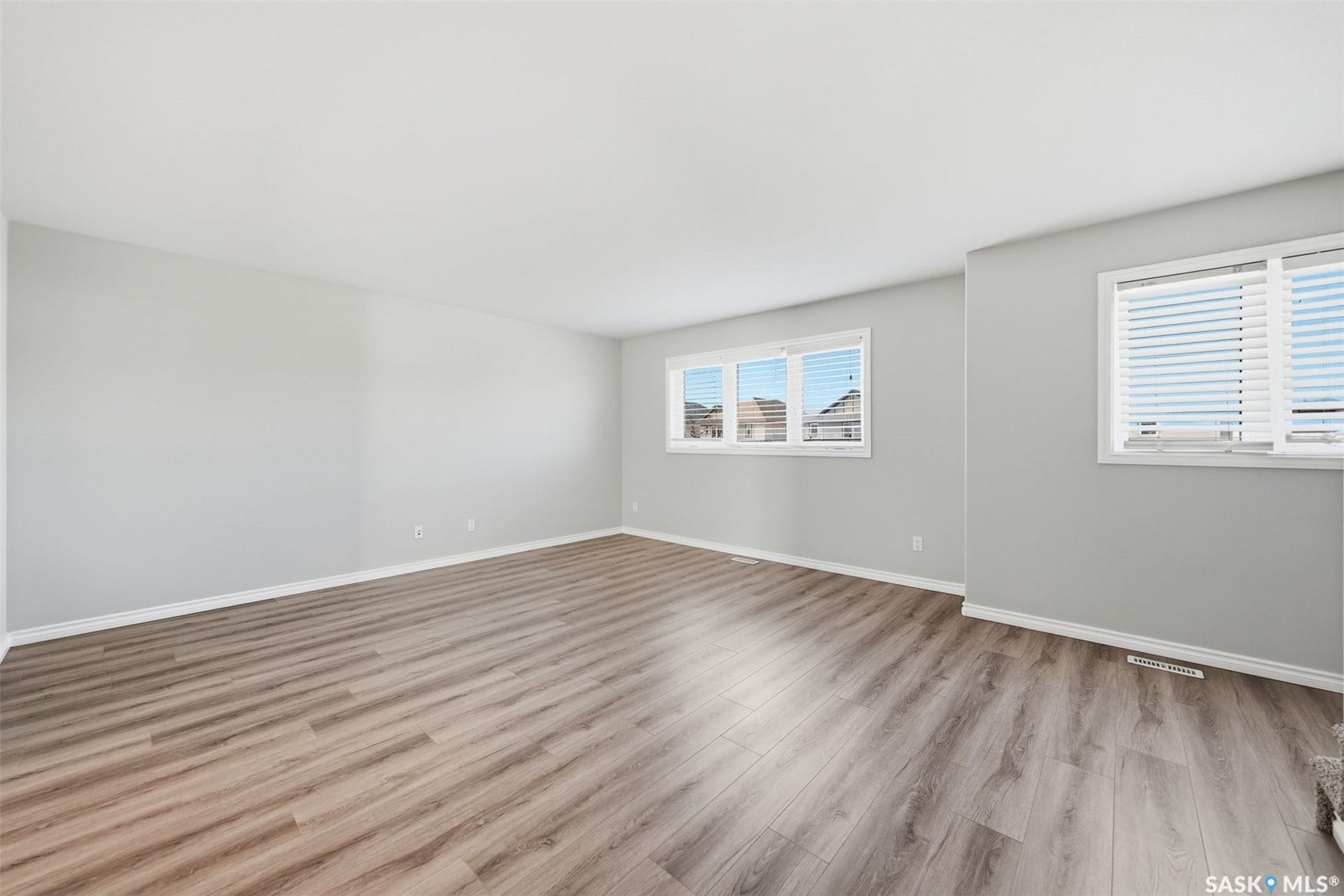 Wood-finish flooring, light gray wall paint, multiple windows with white blinds, and white trim
