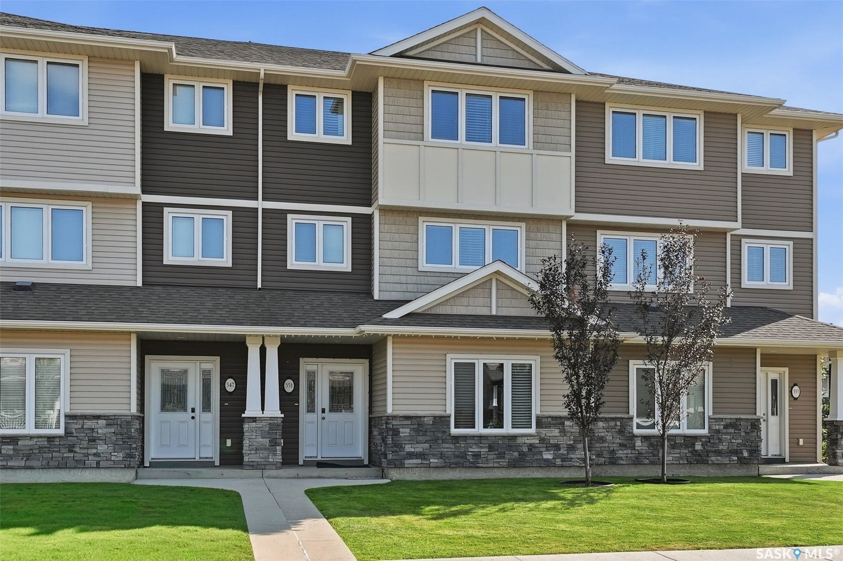 Multi-level exterior featuring varied siding materials, white-framed windows, dark shingle roofing, stone veneer accents, and a well-maintained lawn